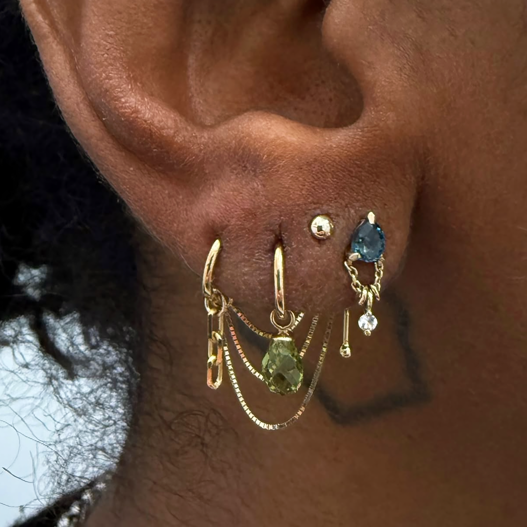A close up of an ear lobe with candy-colored earrings and chain dangles.