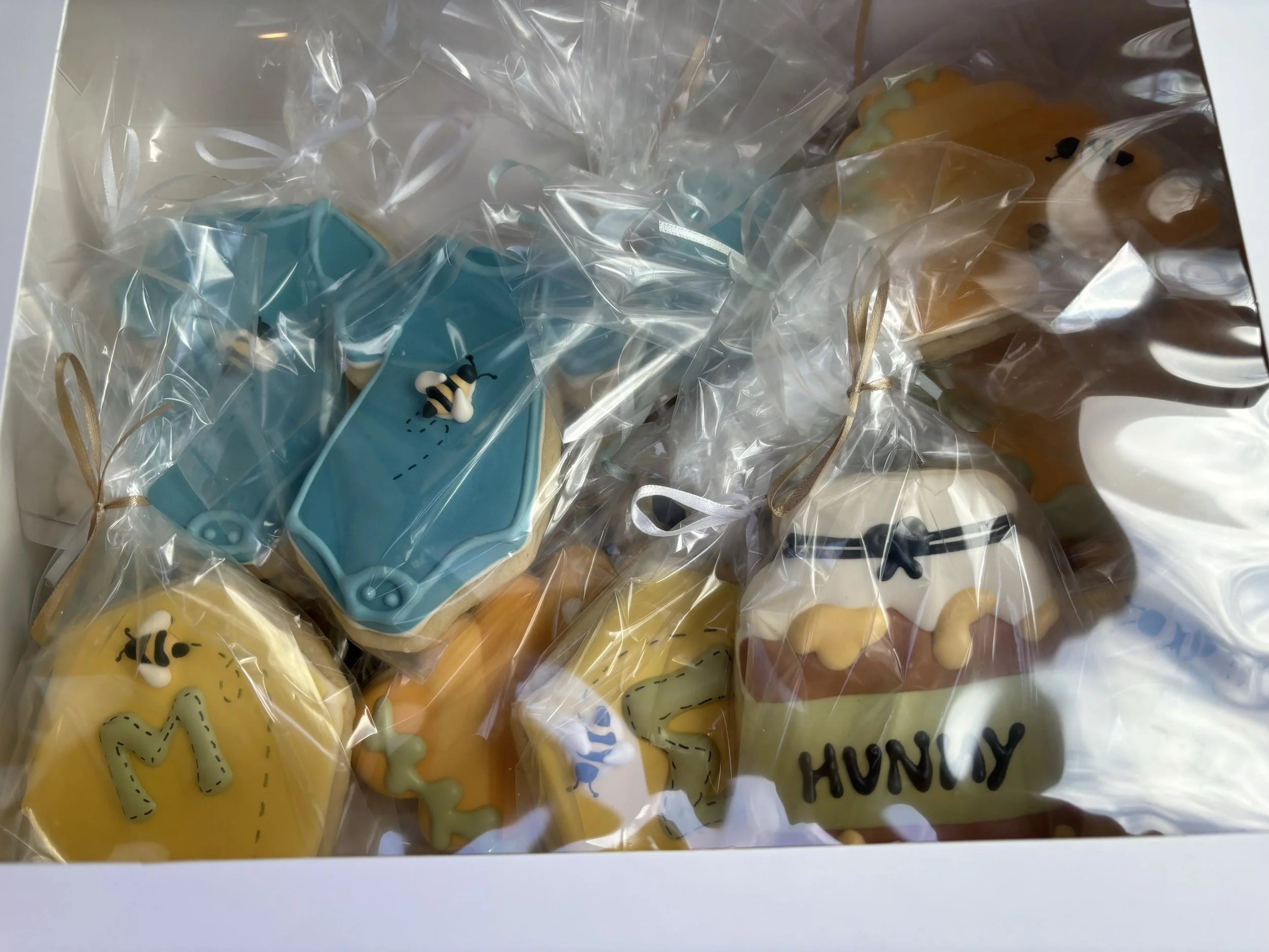 Decorative cookies with bee and honey theme, individually wrapped in plastic with gold ribbons, featuring the words 'Hunny'.