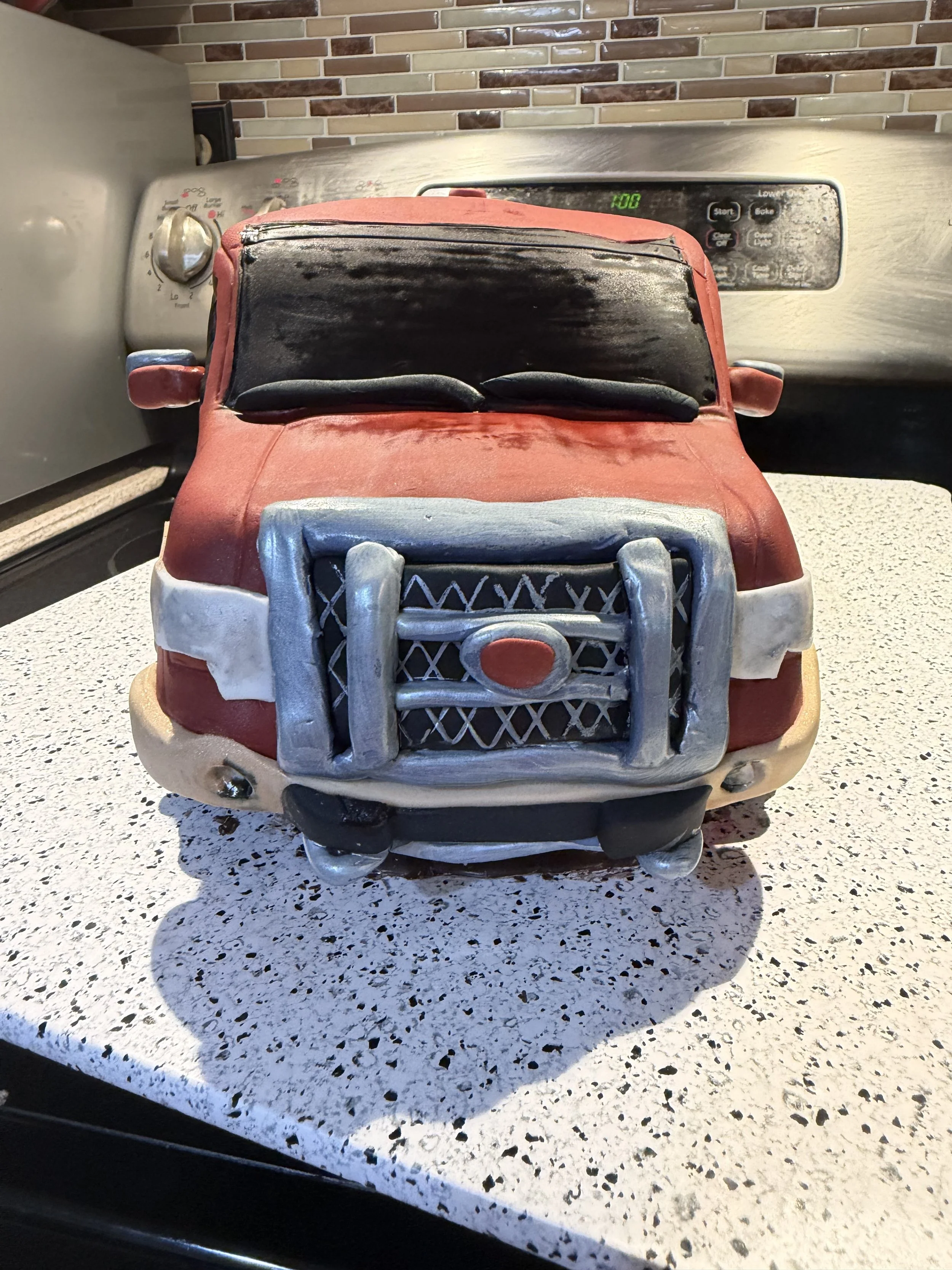 A front view of this custom sculpted pickup truck cake showcases the detailed grille guard, headlights, windshield, and handcrafted edible details that bring this realistic vehicle cake to life.