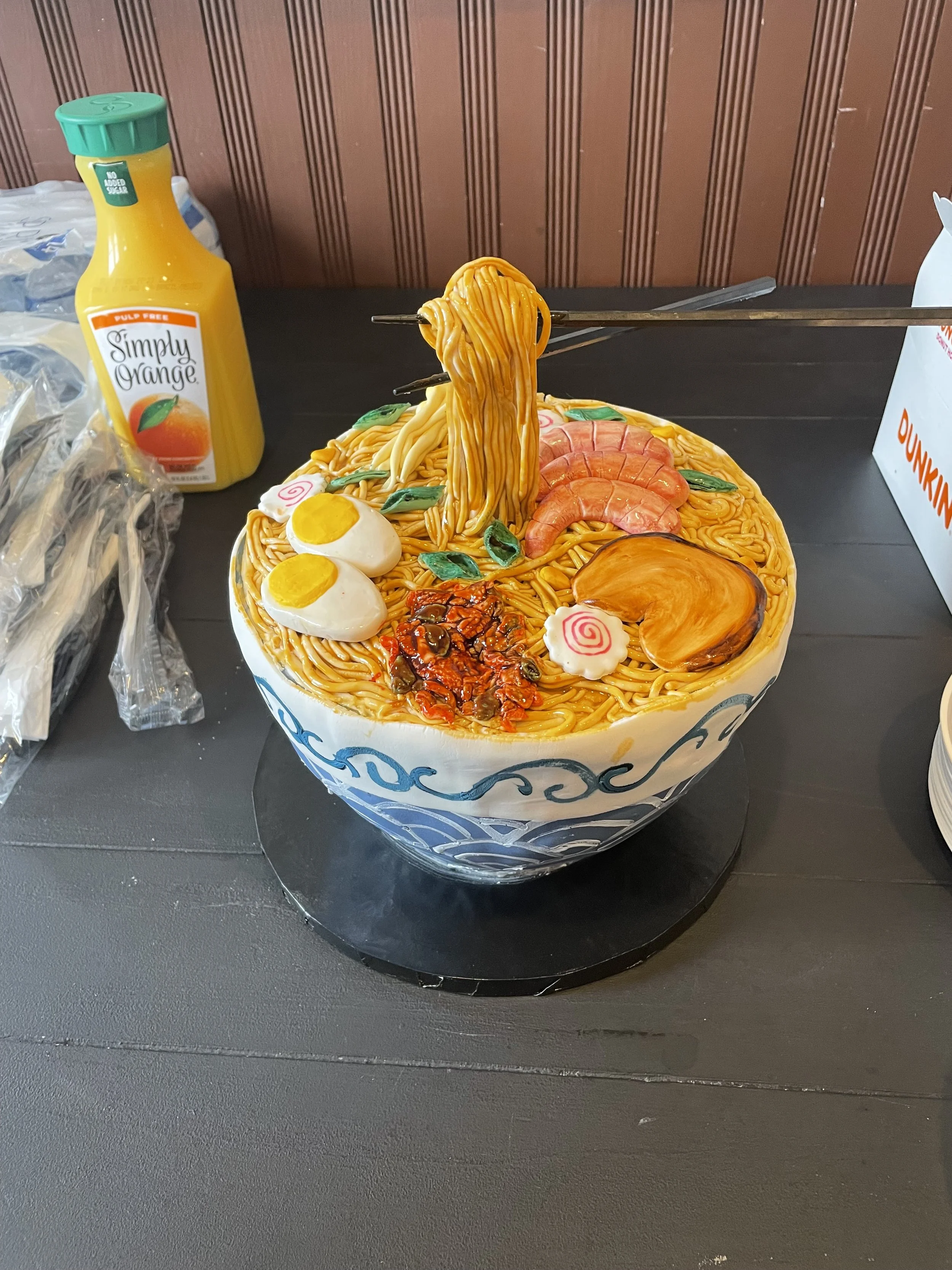 A bowl-shaped cake decorated to look like a bowl of ramen noodles, with noodles, boiled eggs, shrimp, meat, and vegetables made of edible materials.