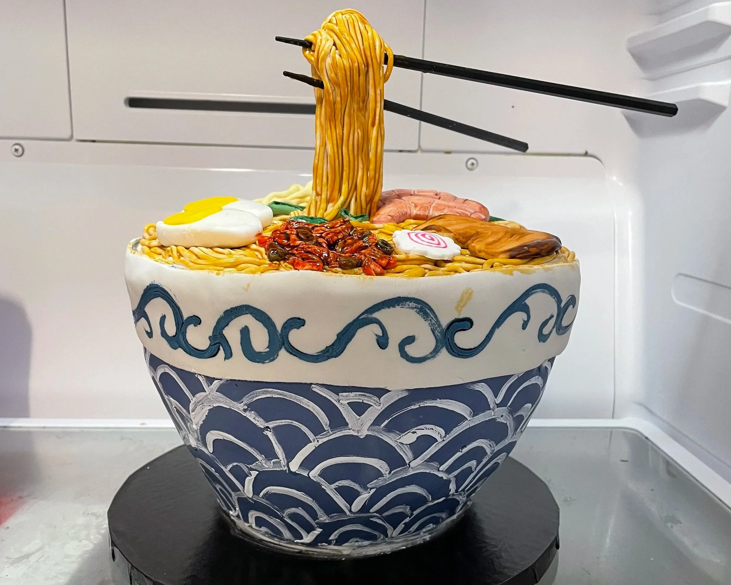 Realistic ramen bowl cake with noodles and chopsticks appearing to lift noodles from the bowl.