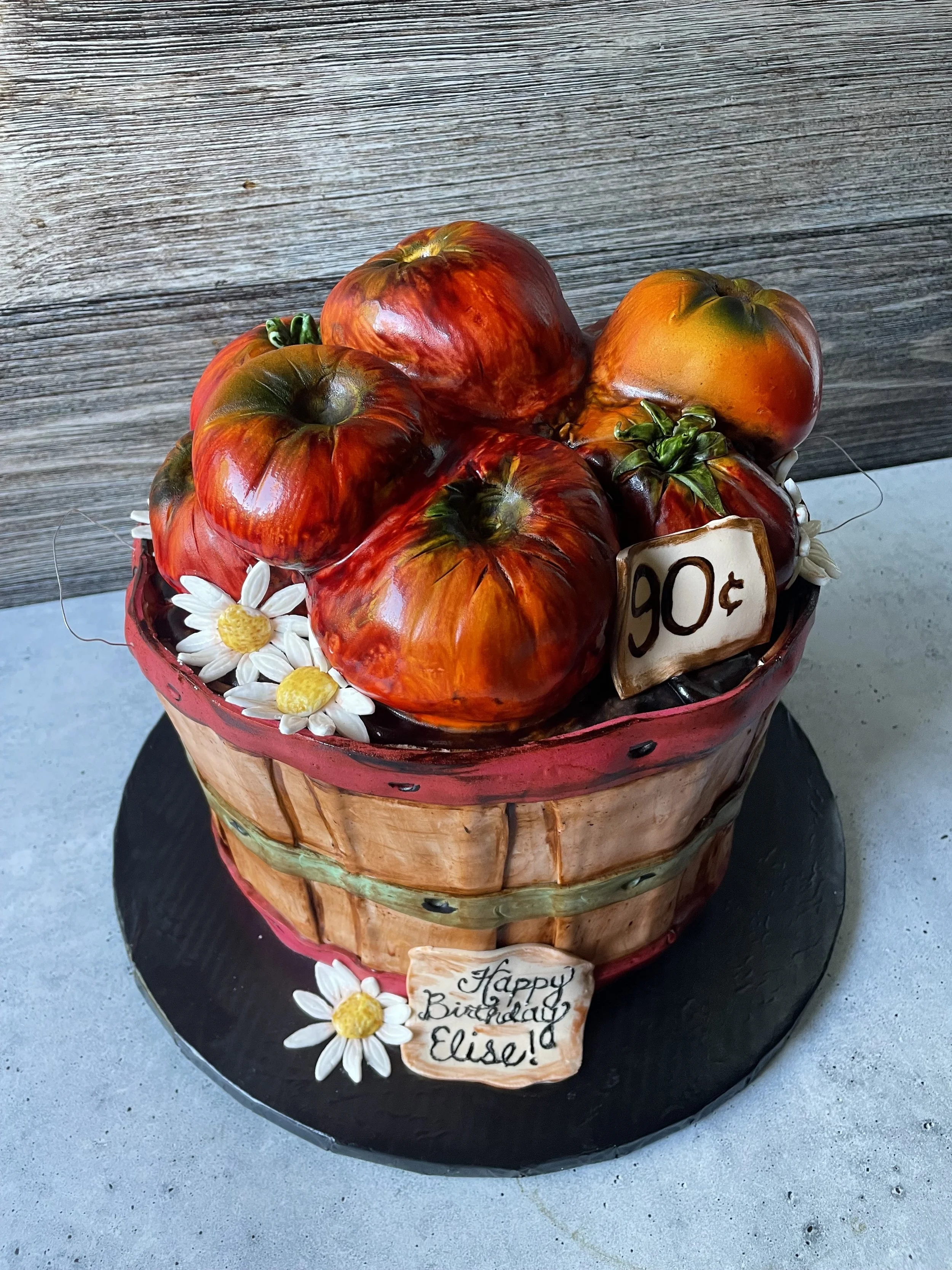 Cake designed to look like a basket of tomatoes with daisies and birthday message.