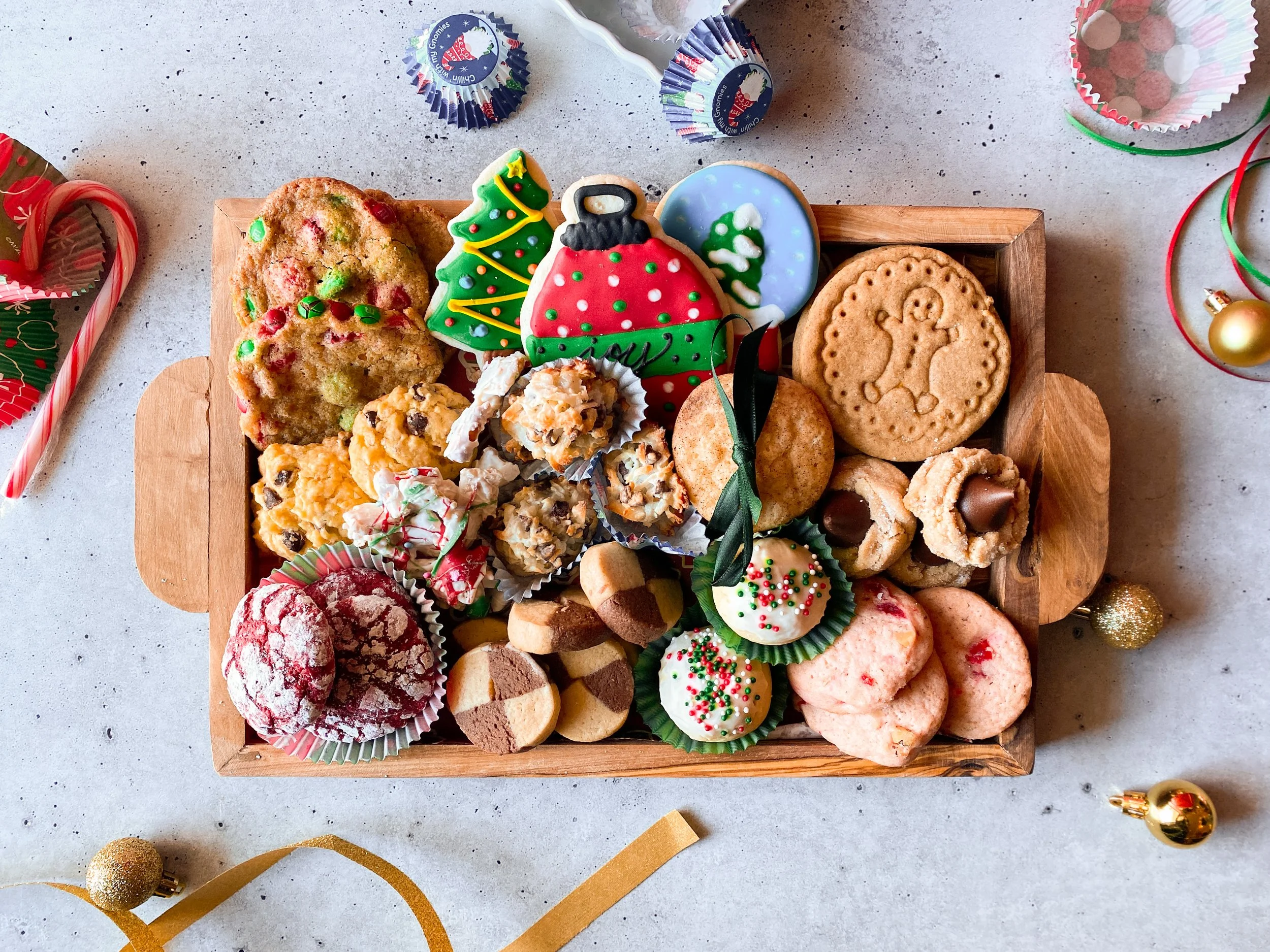 Assorted Christmas cookies and treats on a wooden tray surrounded by holiday decorations.