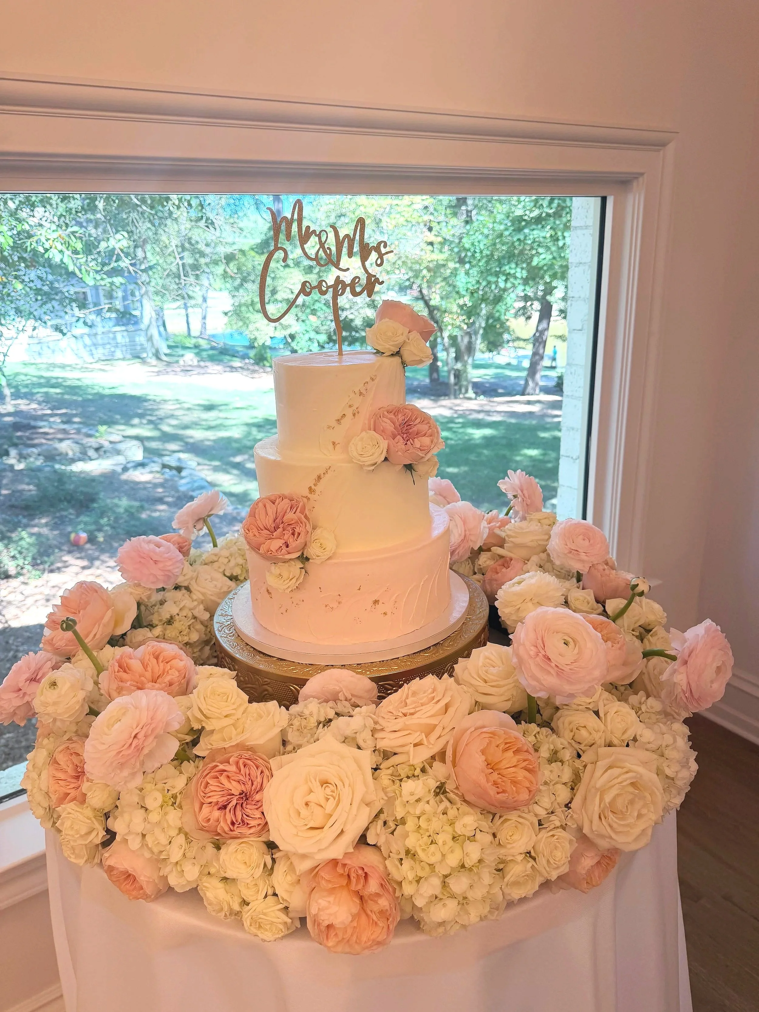 Three tiered blush and white buttercream wedding cake with fresh flowers displayed at Duvall Grounds in Jefferson, Georgia