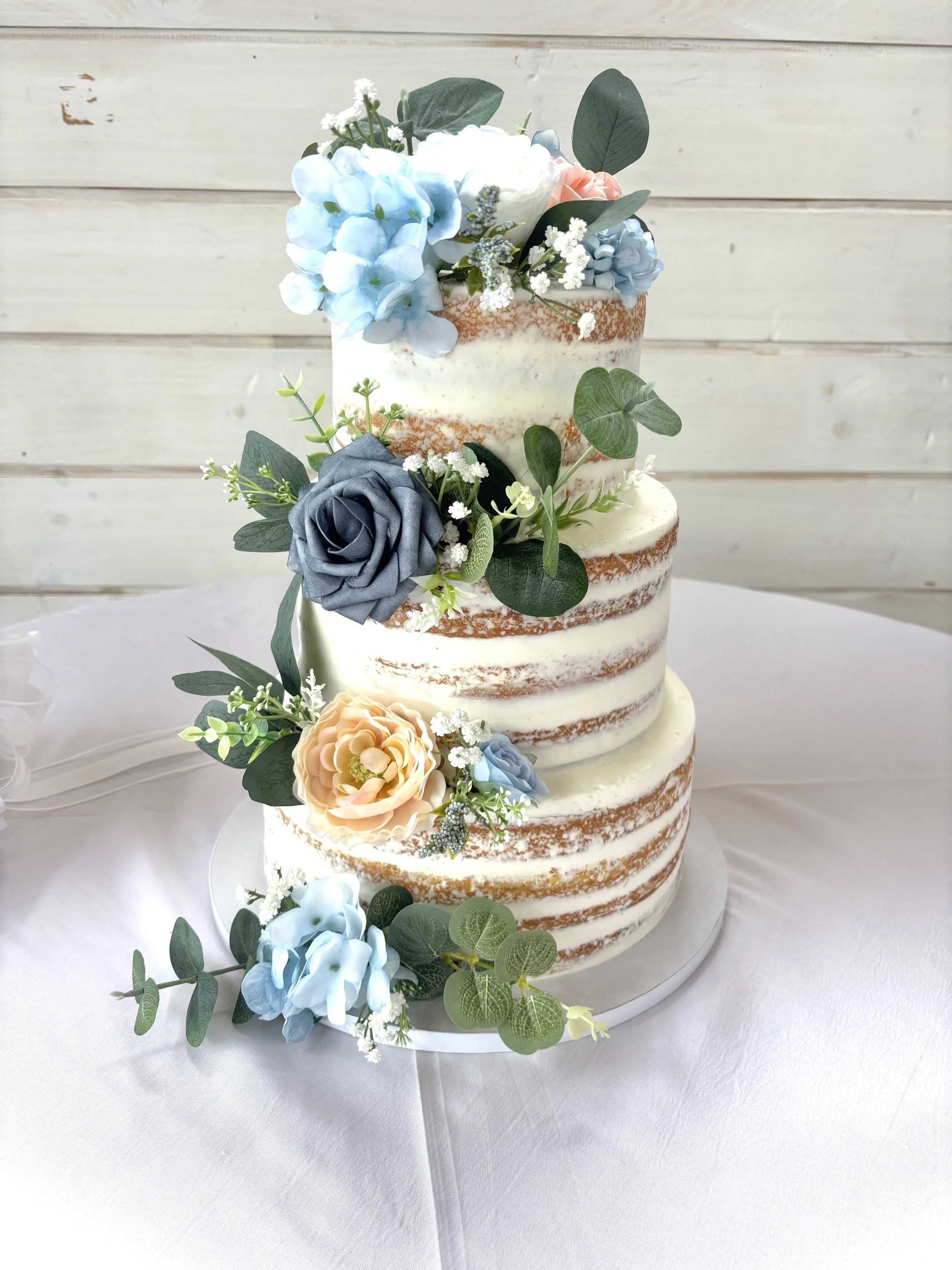 Naked iced 3 tier wedding cake with faux flowers