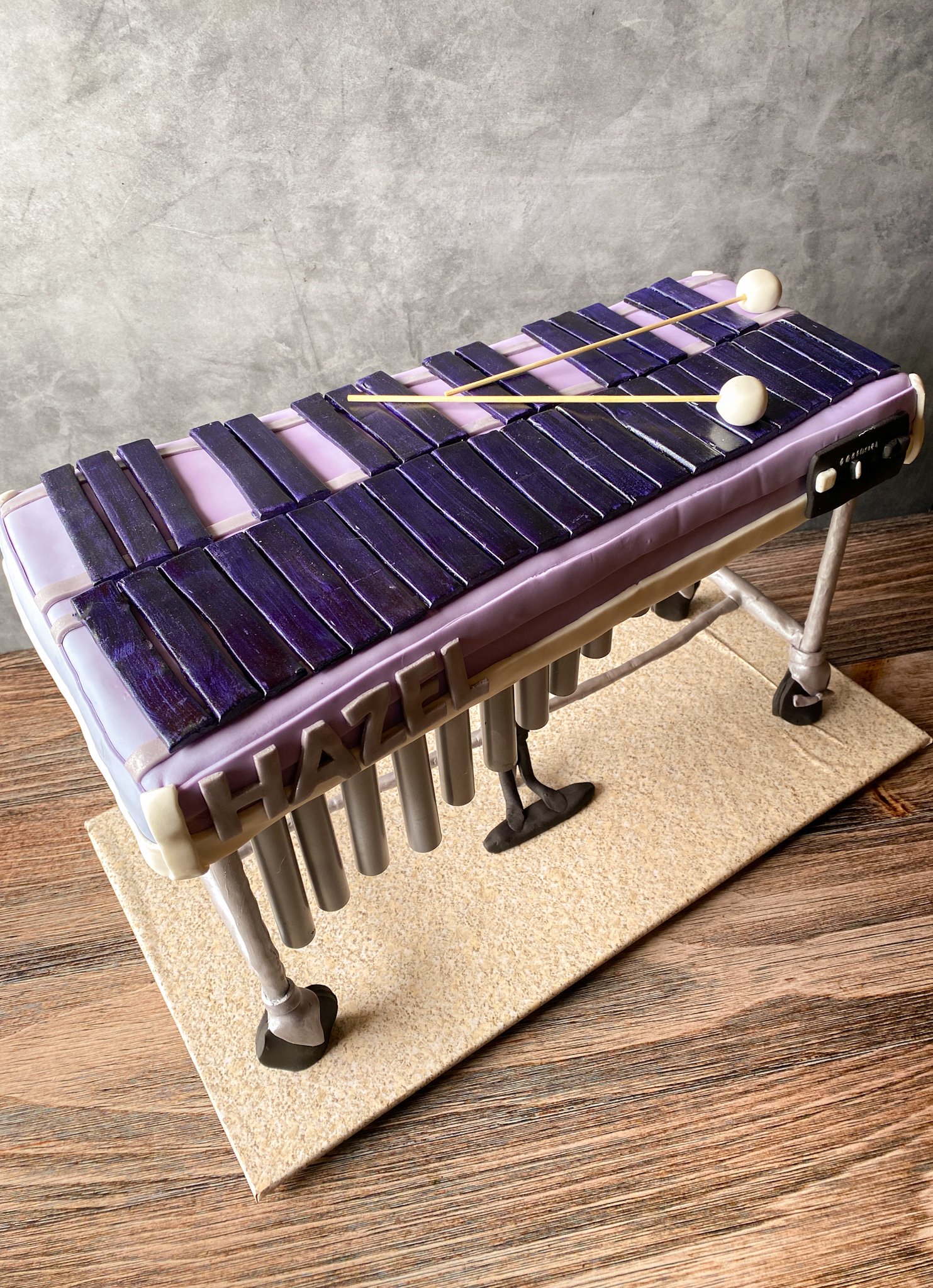 Cake decorated to look like a xylophone with purple keys and white mallets on top, with the name HAZEL spelled out in white letters on the side.