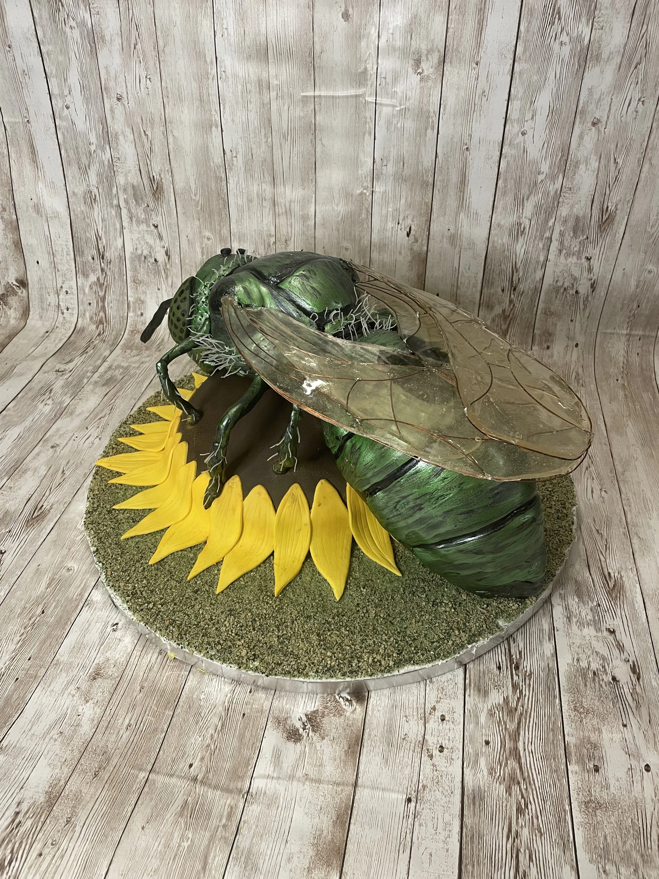 Realistic cake of a green metallic sweat bee on a sunflower, with edible moss base