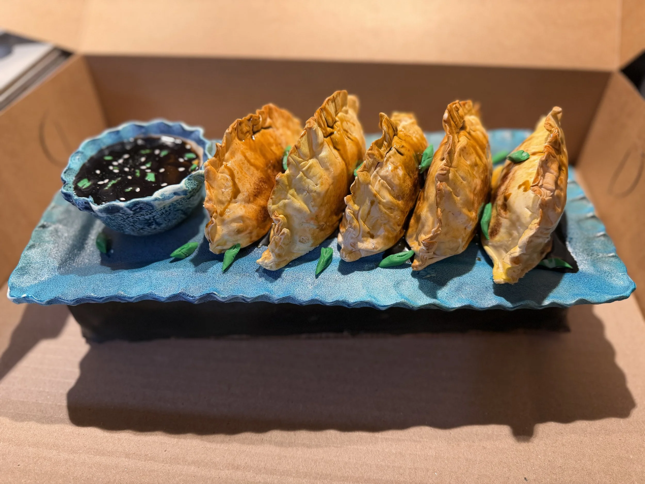 Is it dinner or dessert? This realistic gyoza cake features five sculpted fried dumplings served with an edible dipping sauce bowl on a completely edible blue platter.