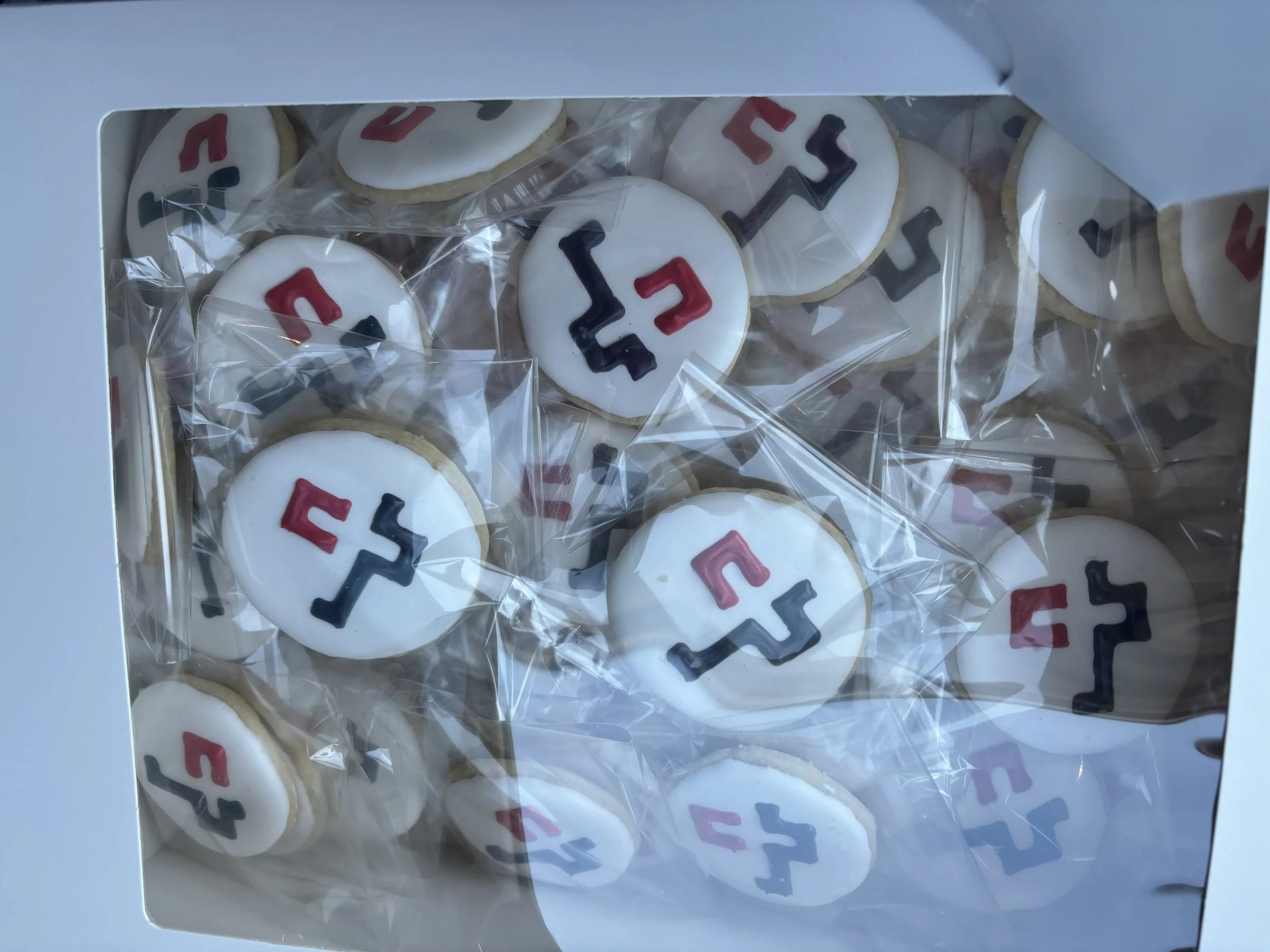 Cookies with white icing and a logo featuring red, black, and pink elements inside a white box with a clear top.
