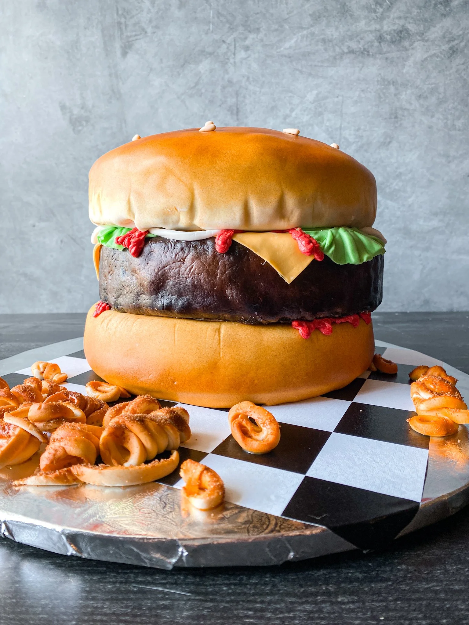 Realistic cheeseburger cake designed and decorated by Julie McDaniel at Artful Cakery by Julie at her bakery in Flowery Branch, Georgia fondant curly fries sesame seeds ketchup lettuce cheese custom bakery cakes - North Georgia Bakery 