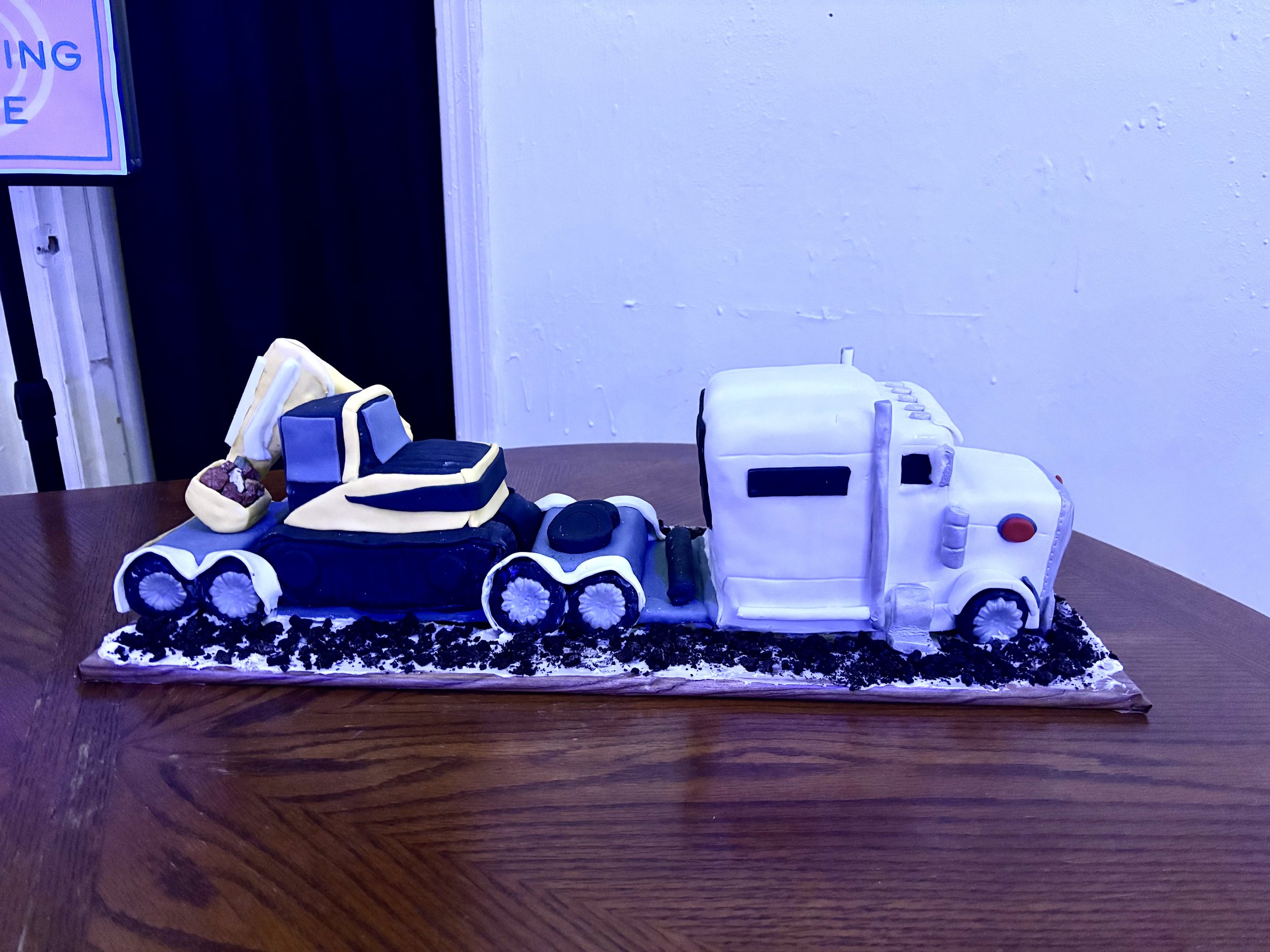 Sculpted Peterbilt truck cake with flatbed trailer carrying an excavator.