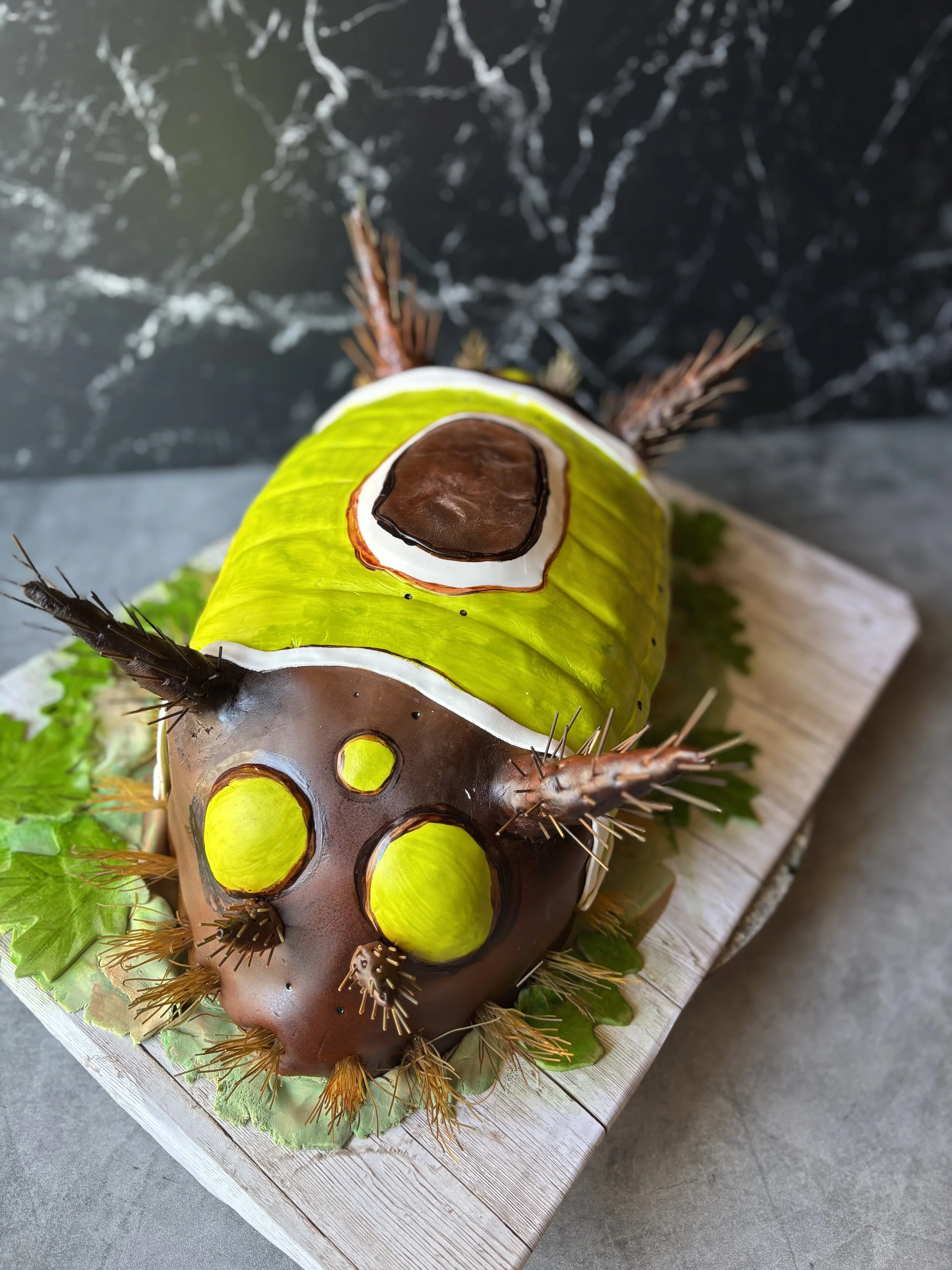 Realistic saddleback caterpillar cake with spines and colorful markings.
