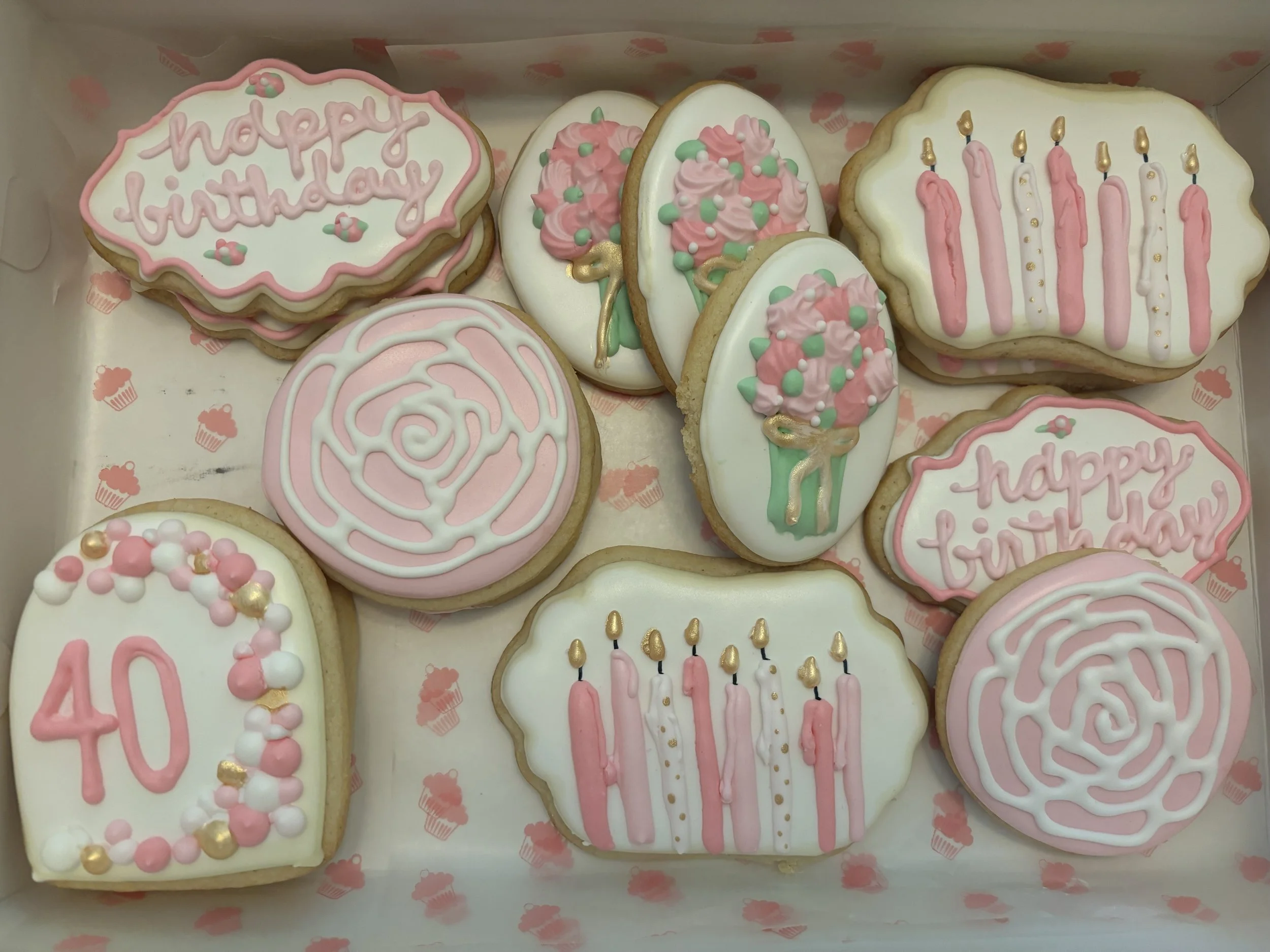 Decorated birthday cookies with pink and white icing, some with the number 40, some with candles, and some with 'happy birthday' messages.