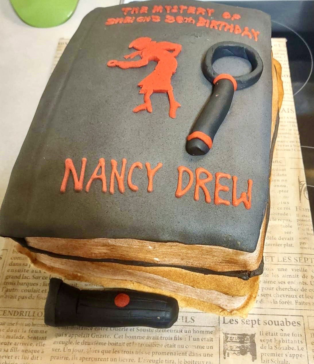 Stack of Nancy Drew books cake with flashlight and magnifying glass designed as a realistic book-themed cake.