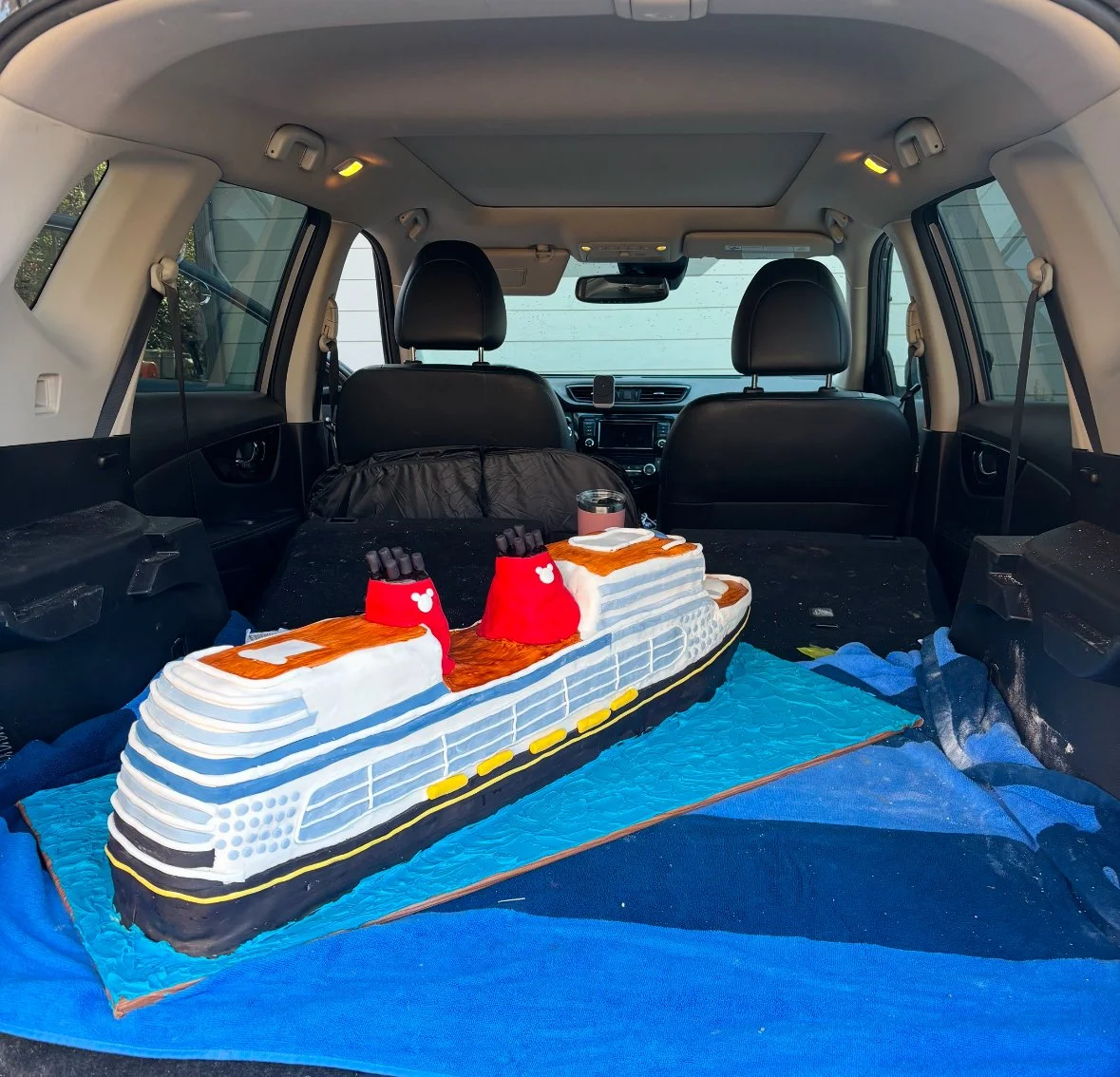 Cake shaped like a cruise ship inside the back of a vehicle.