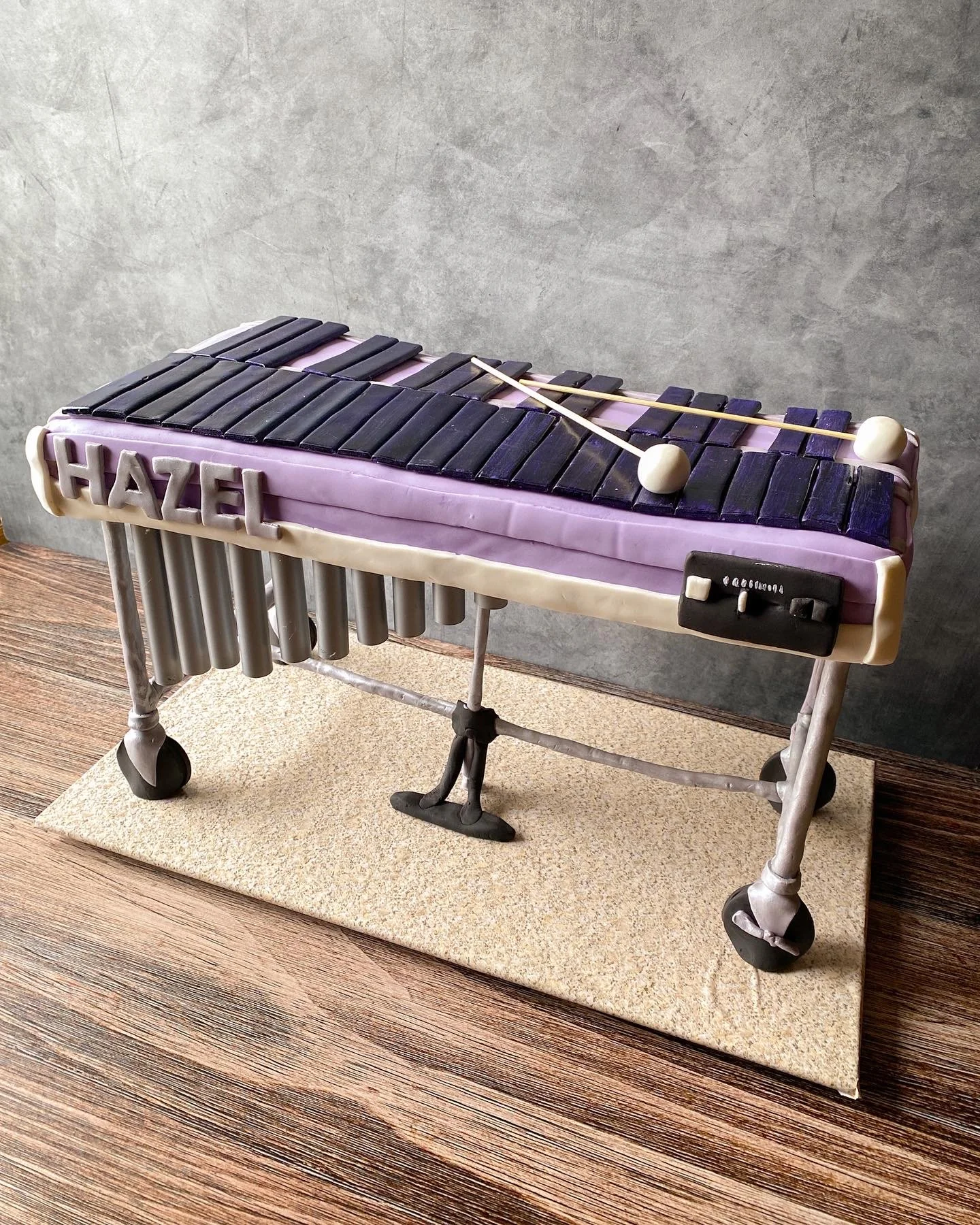 A cake shaped like a vibraphone with purple, black, and white icing, featuring the name 'Hazel' on the side.