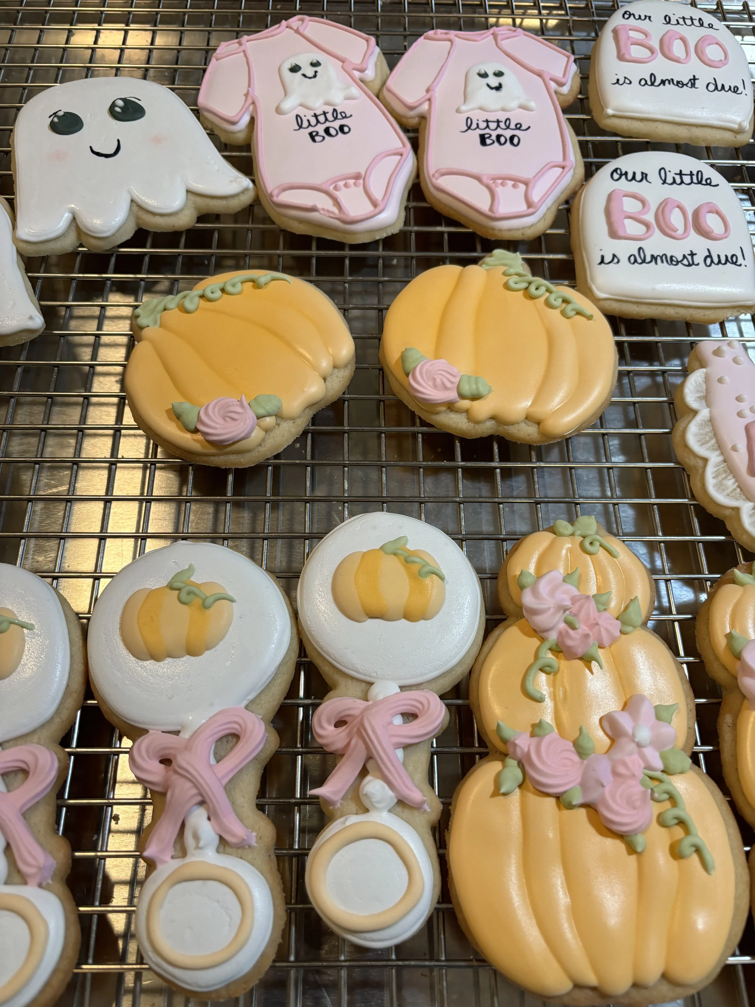 Halloween-themed decorated sugar cookies with pumpkins, ghosts, and signs saying "Our little BOO is almost due!"