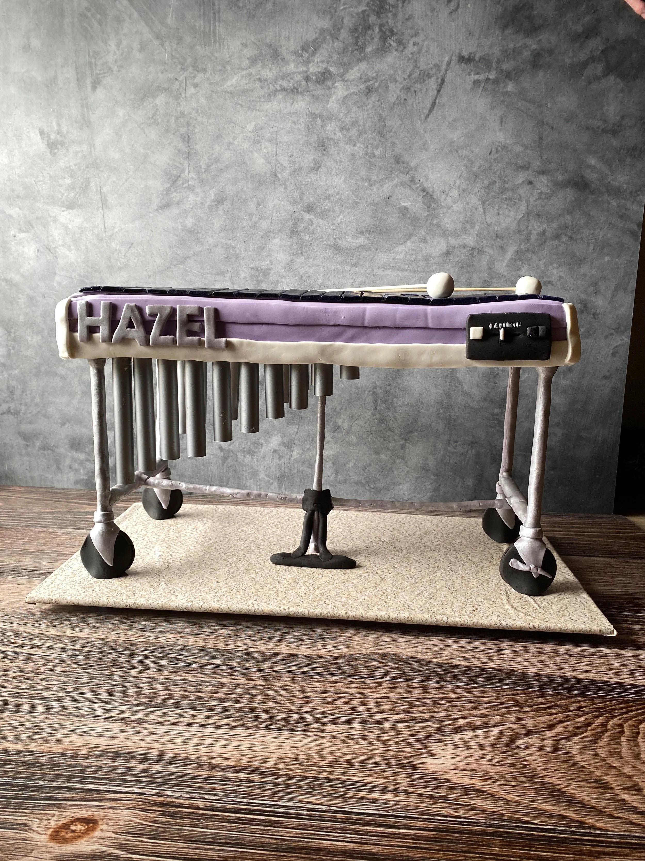 A cake decorated as a xylophone with black and white keys, metal bars, and a black switch, with the name "Hazel" on the side.