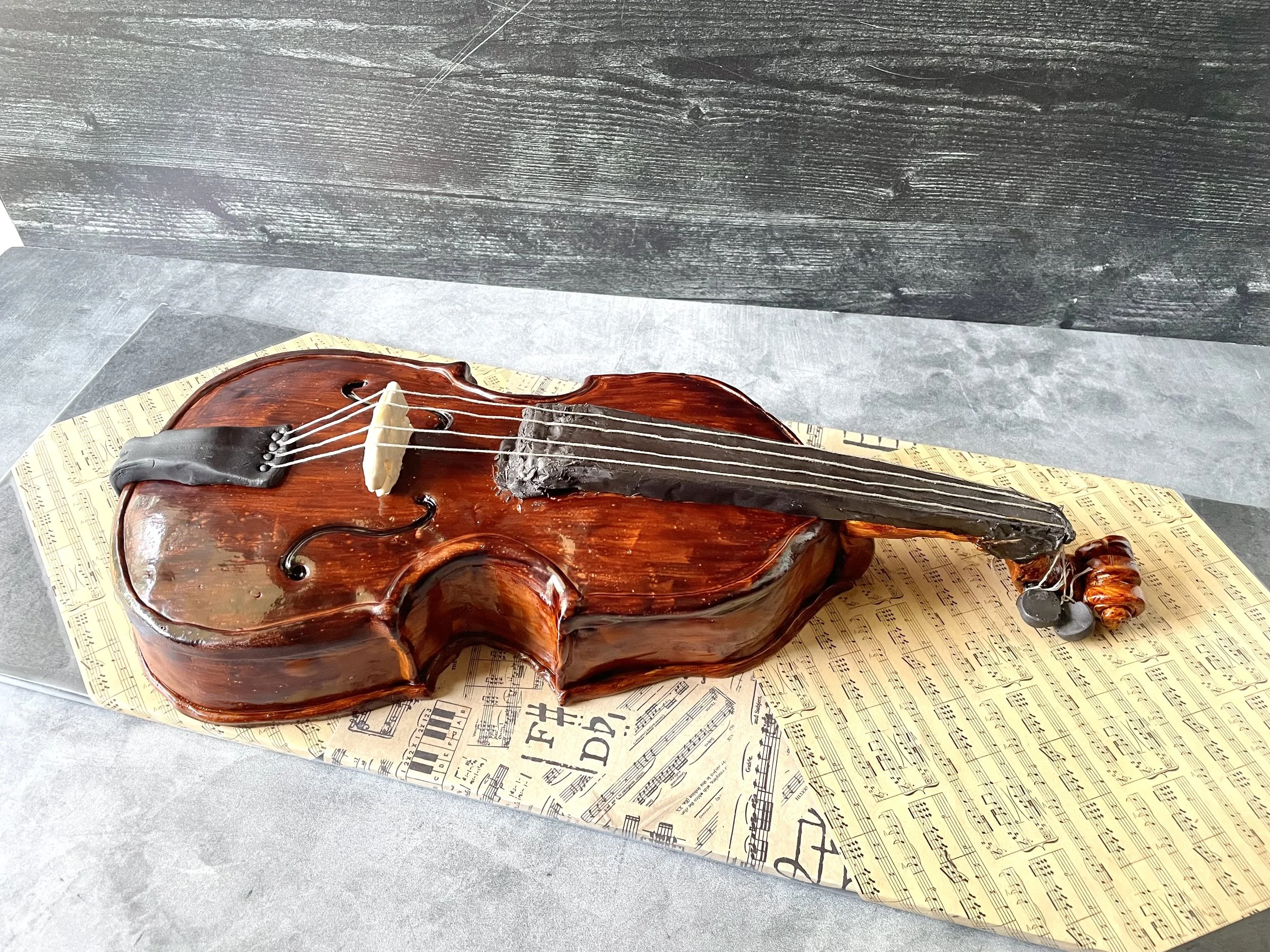 Cake shaped like a violin with musical notes on paper underneath.