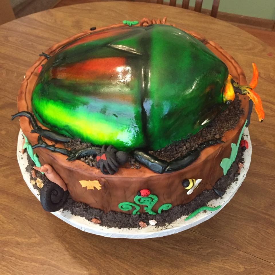 Vibrant beetle sculpted cake on tree stump with detailed edible insects