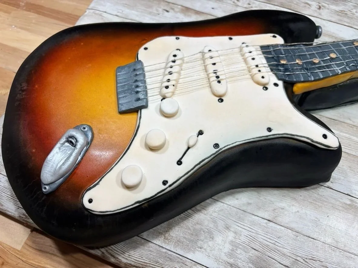 A guitar-shaped cake designed to resemble an electric guitar, with a sunburst finish, white pickguard