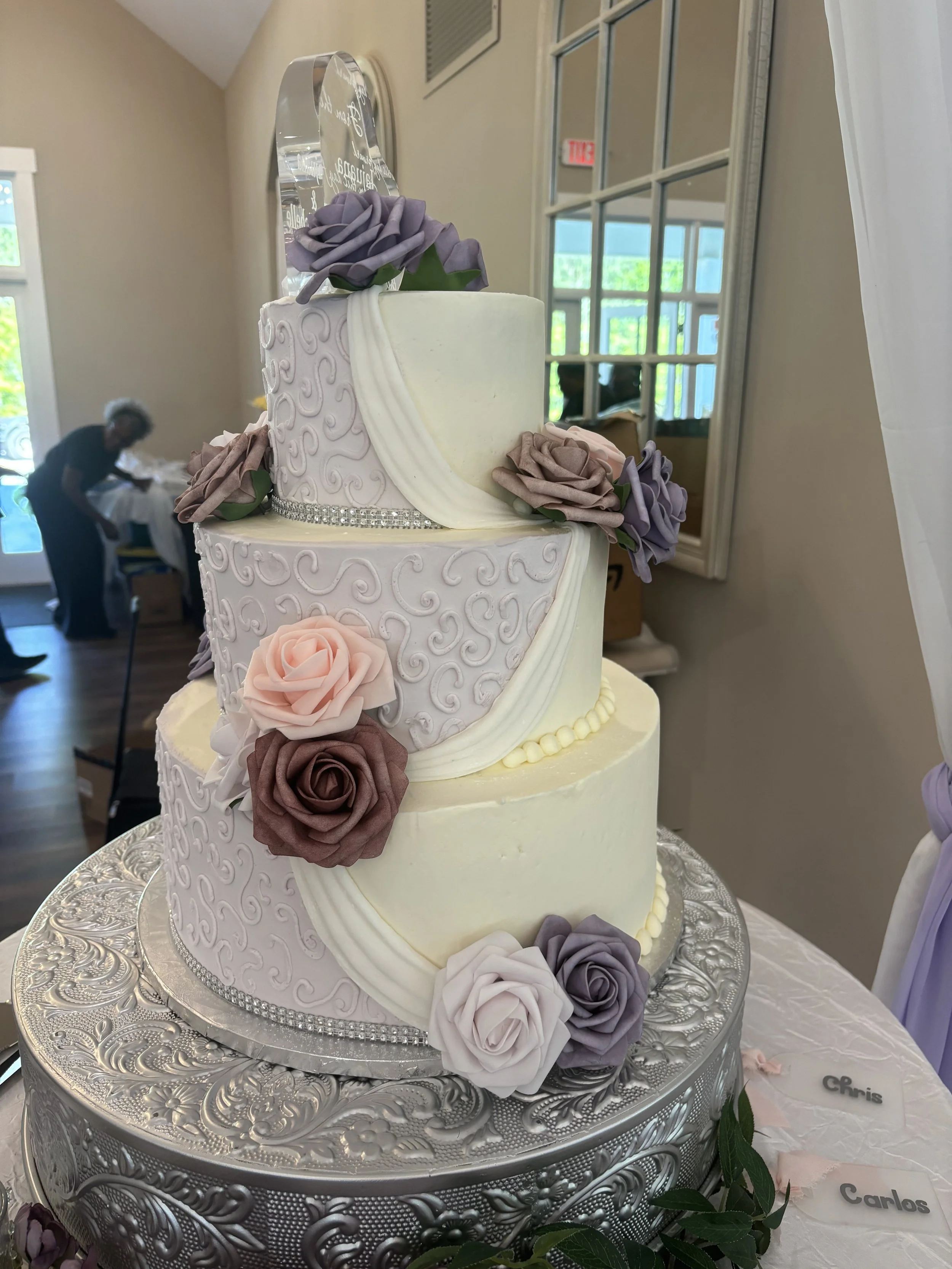 Three tiered buttercream Atlanta wedding cake with lilac and white frosting and assorted pink and purple artificial flowers at Whitestone Reserve Wedding venue in Austell, GA