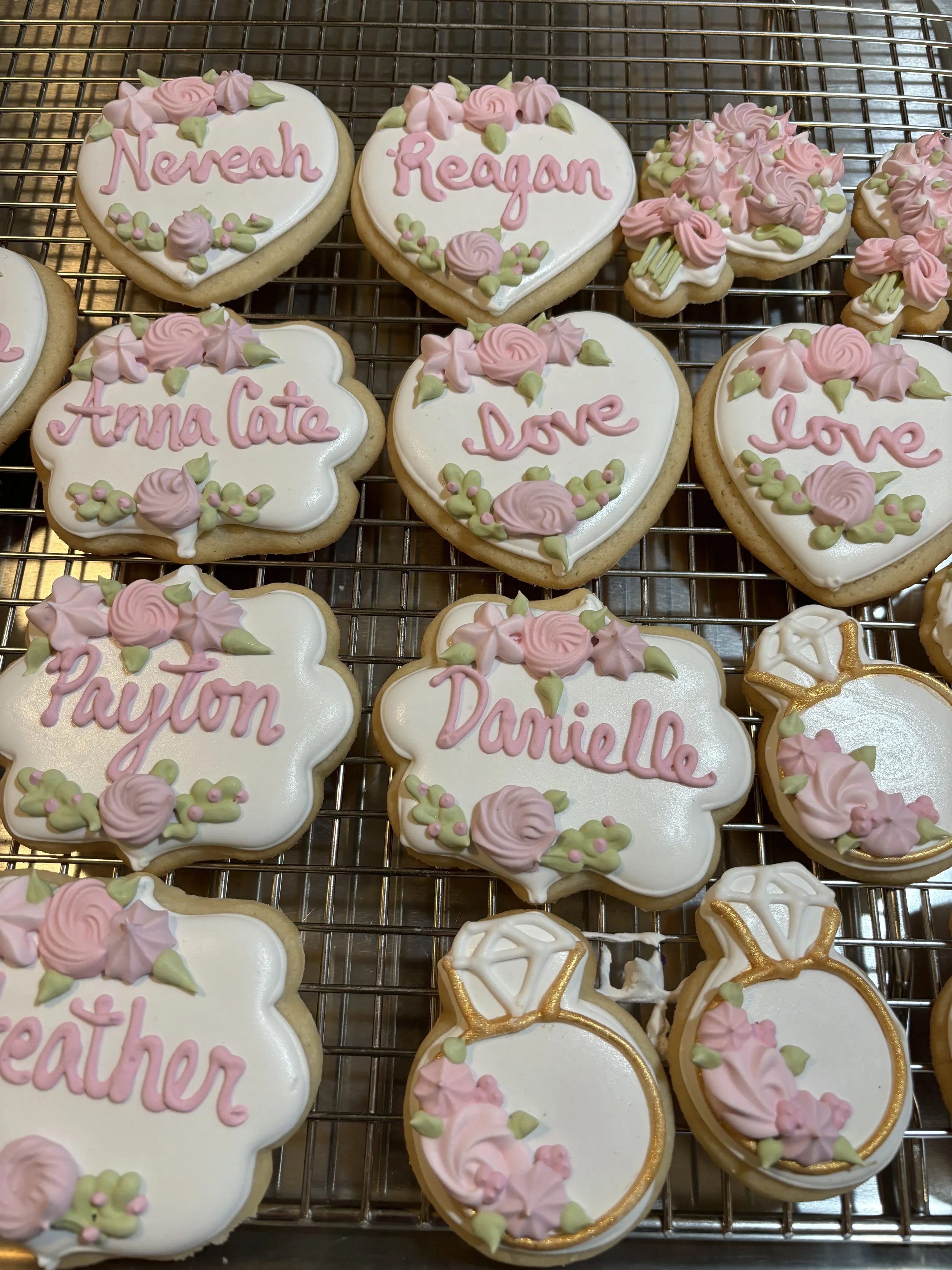 Decorated cookies with floral pink and green icing, some heart-shaped, some flower-shaped, with names written on them