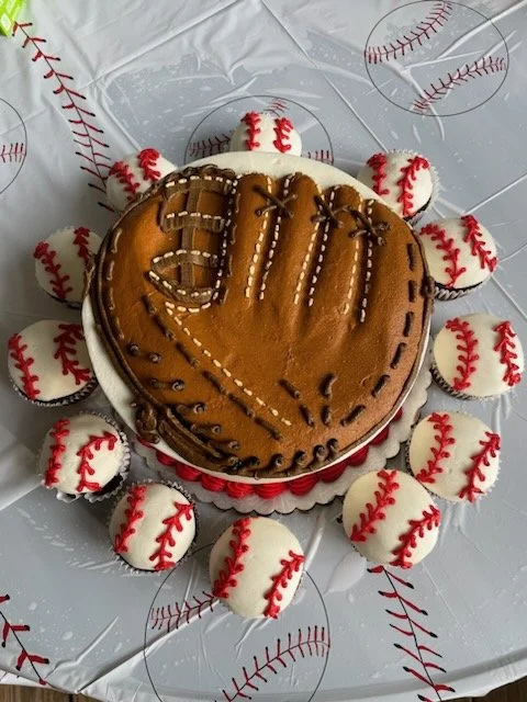 Sculpted baseball glove cake with baseball cupcakes for a baseball-themed celebration.
