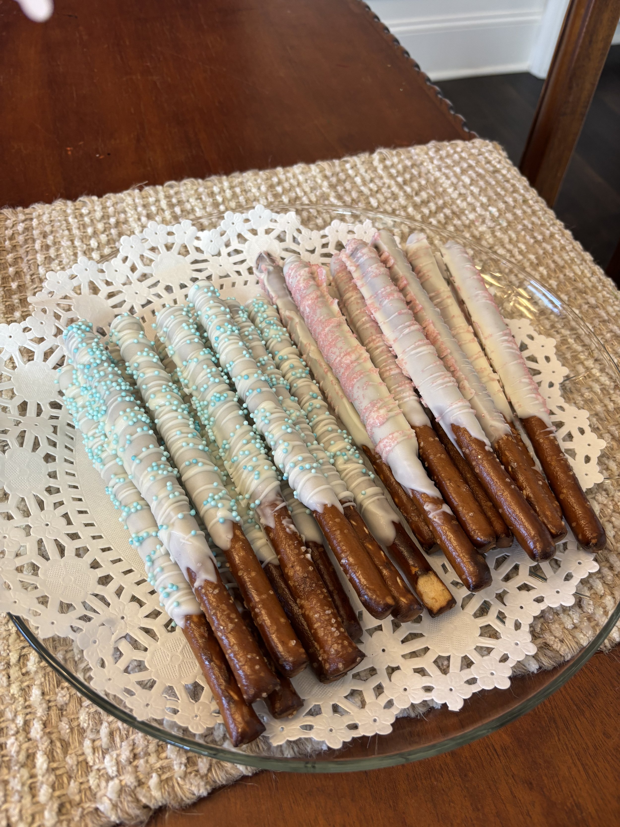 White chocolate dipped pretzel rods with blue and pink accents for a gender reveal party