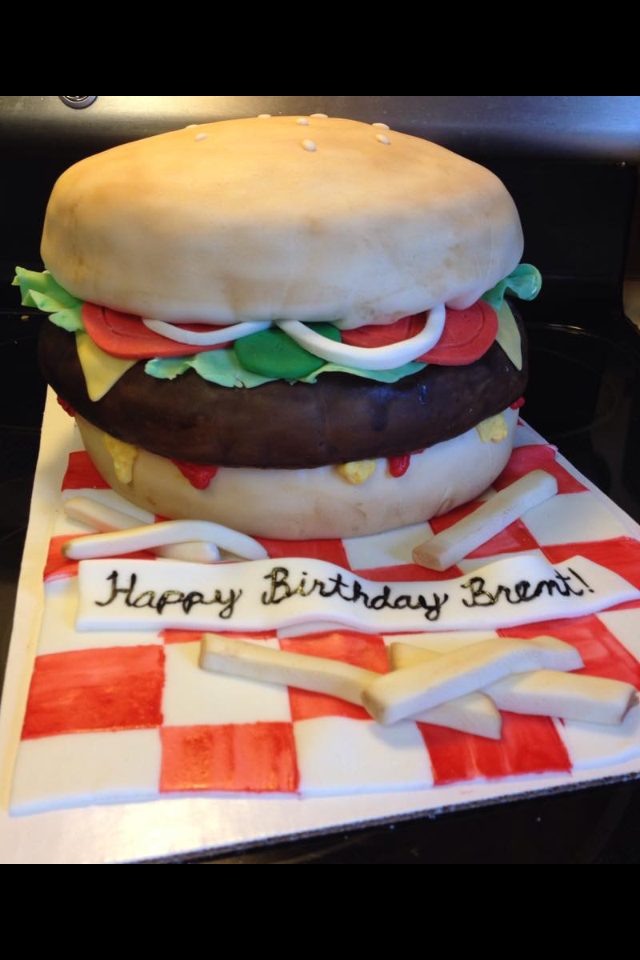 Hyper-realistic hamburger cake with bun, lettuce, and tomato designed to look like a real burger.