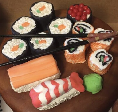 Assorted sushi rolls with cucumber, carrot, and cream cheese, topped with red fish roe, and decorative sushi resembling a shrimp all on a wooden plate with chopsticks. 