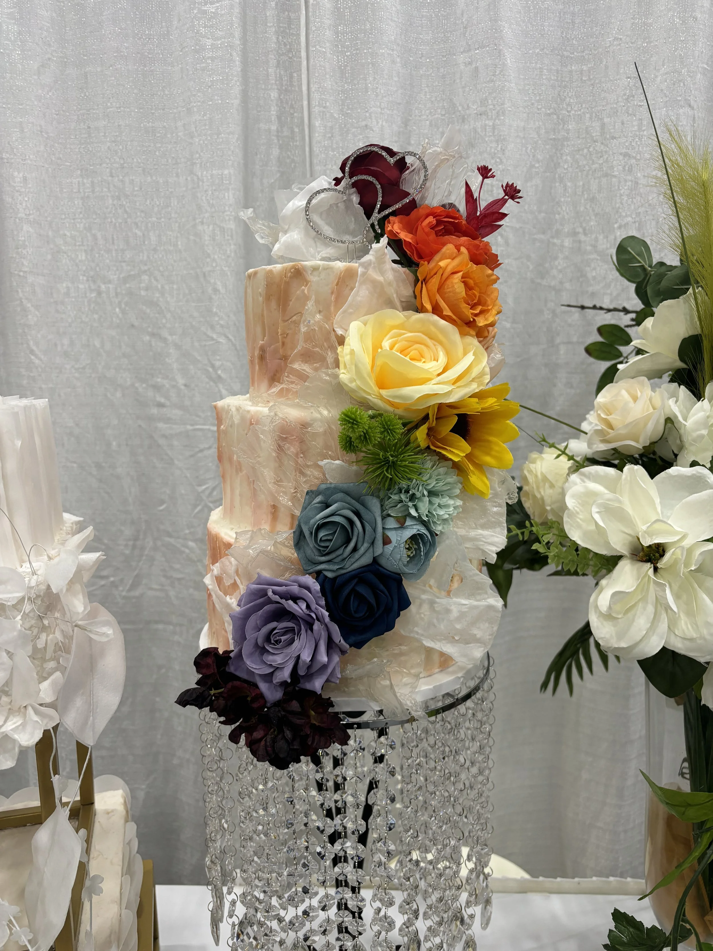 Decorative cake with colorful flowers on top, displayed on a stand with crystal bead curtain.