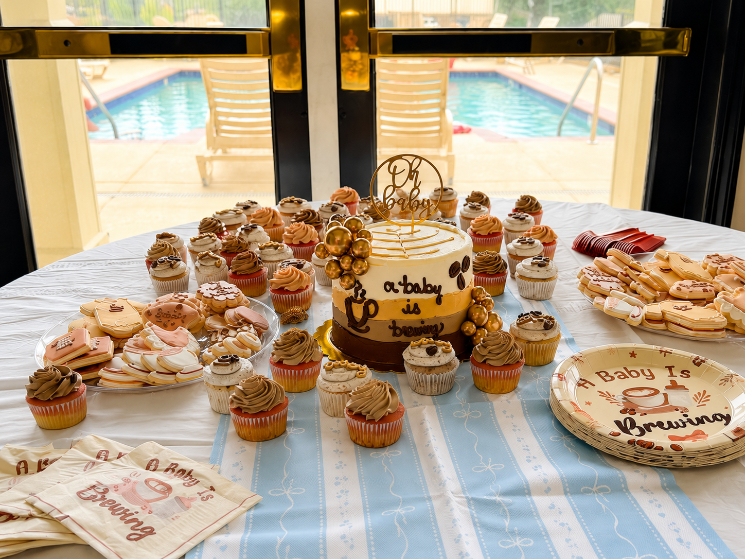 a baby is brewing cake, cupcakes, and decorated sugar cookies