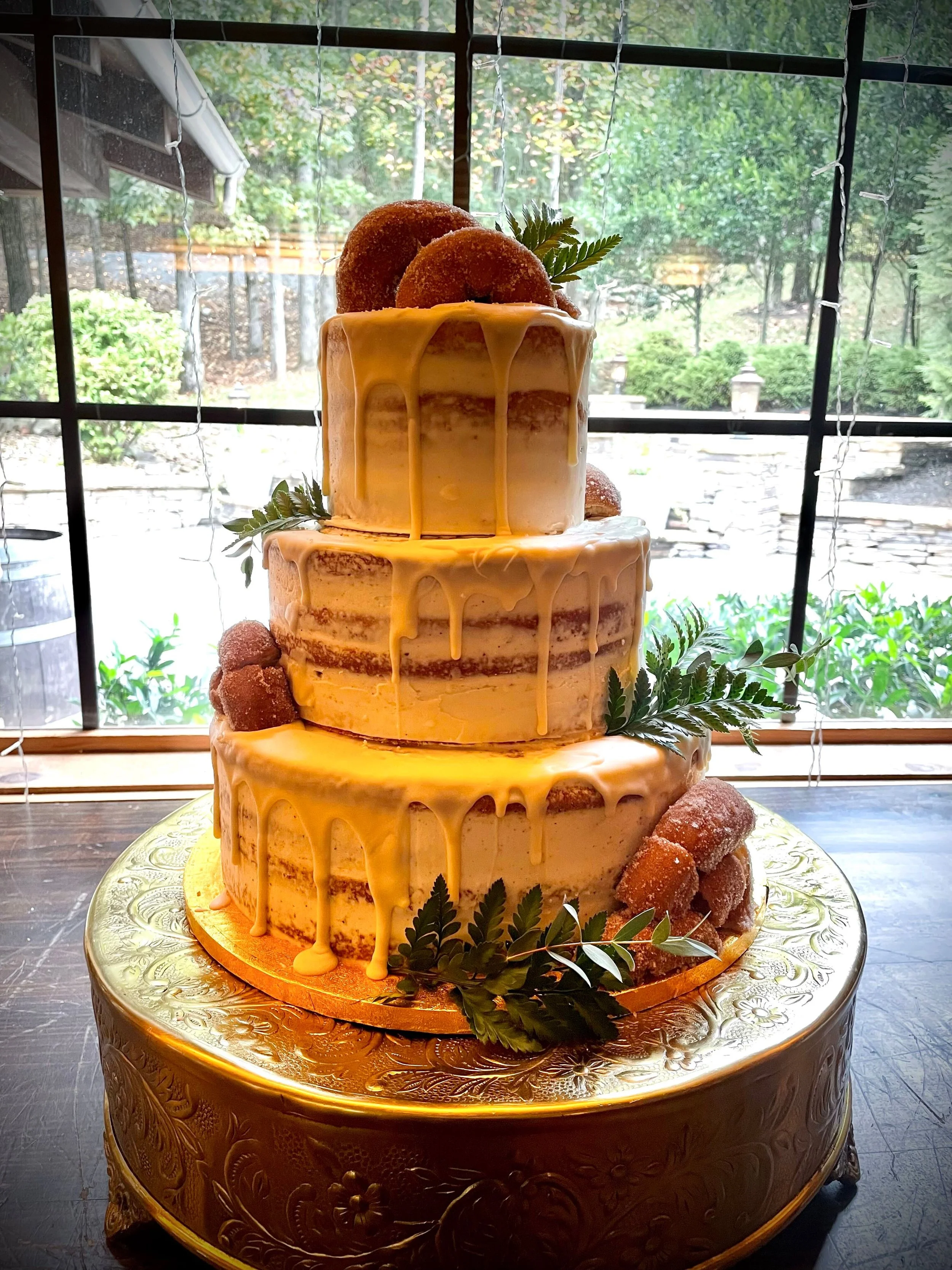 Three tiered naked iced wedding cake in spiced apple cider with apple pie filling, brown butter frosting, caramel drizzle, and apple cider donut decorations
