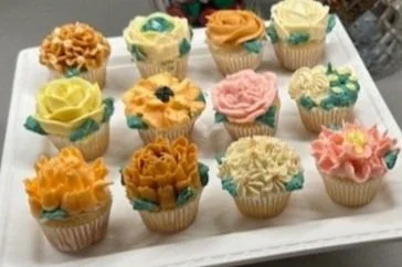 A tray of 15 decorated cupcakes with colorful frosting and flower-shaped decorations.