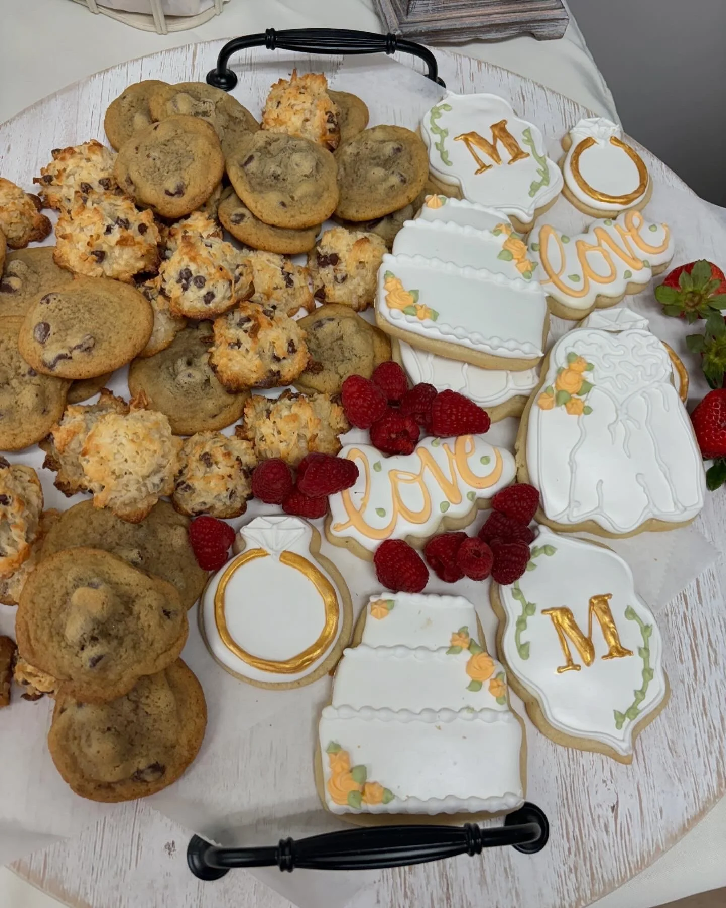 Cookie platter with chocolate chip cookies, coconut cookies, decorated cookies with love and M initials, fresh raspberries, and strawberries on a white tray.