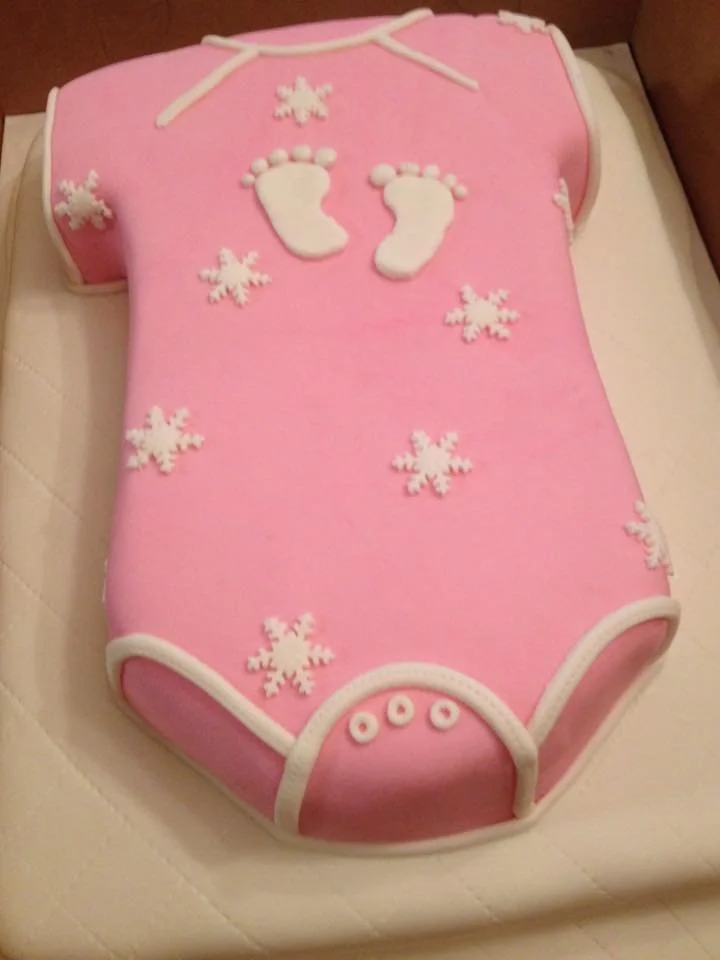 Sculpted pink baby onesie cake with white footprints for baby celebration