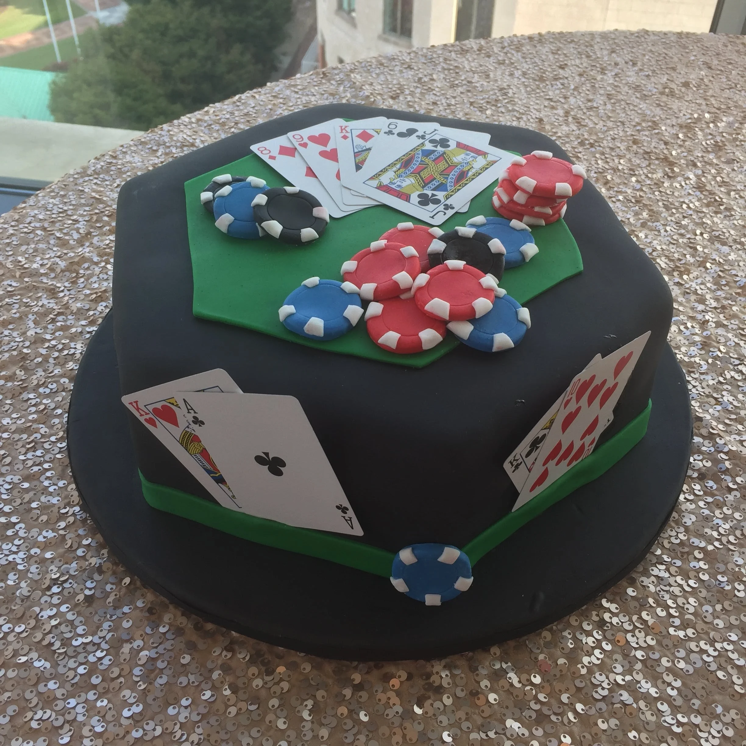 A cake decorated with poker chips, playing cards, and a green felt mat, celebrating a poker or casino theme.