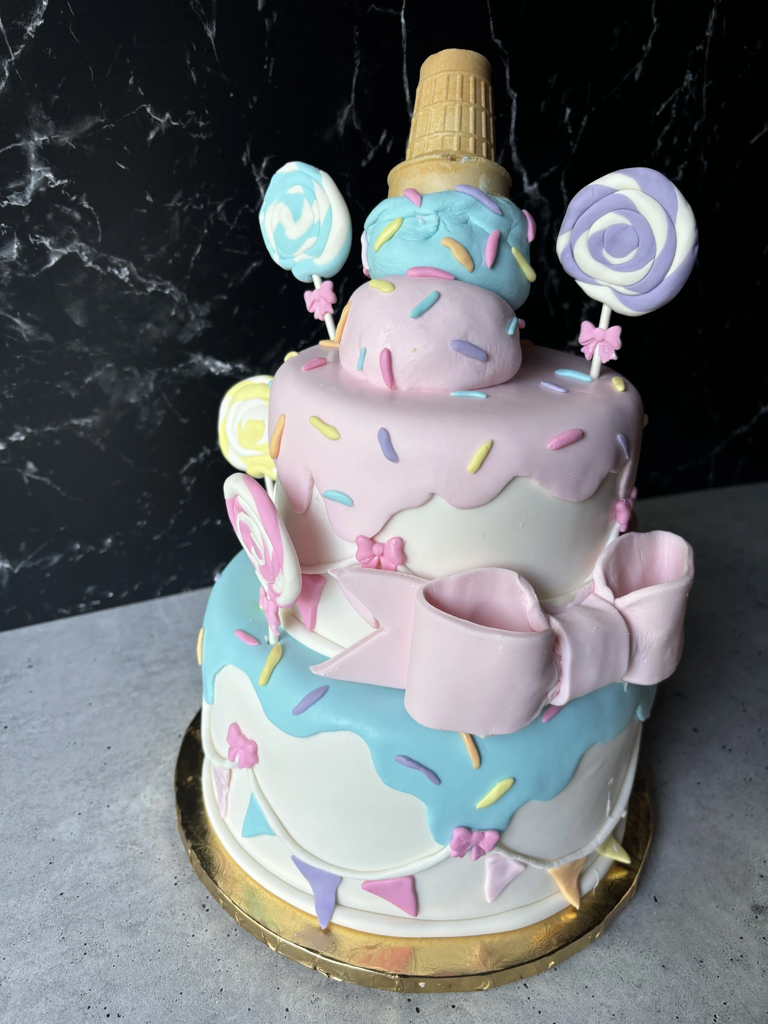 Colorful first birthday cake decorated with ice cream cones and lollipops.