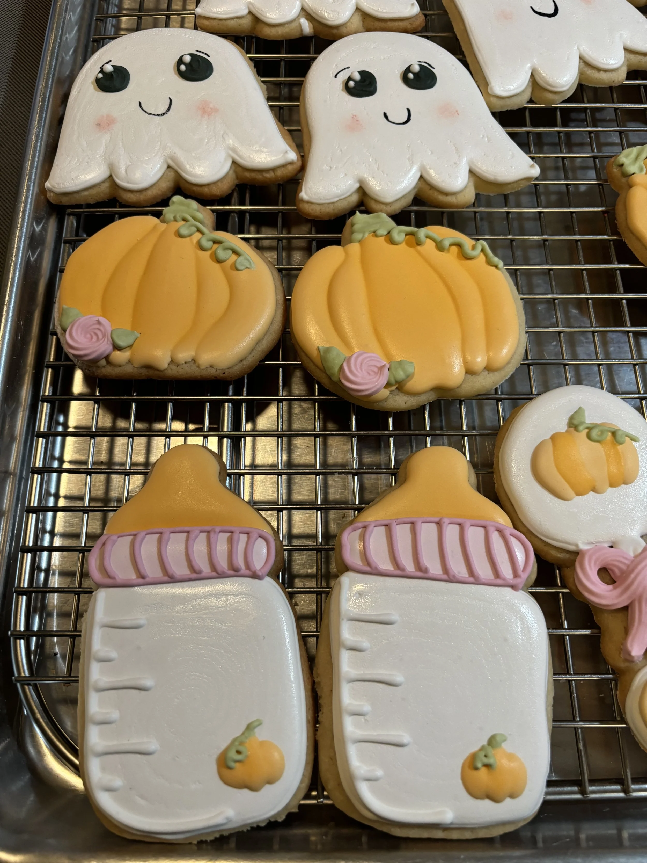 Halloween-themed sugar cookies decorated with ghost, pumpkin, and baby bottle designs.