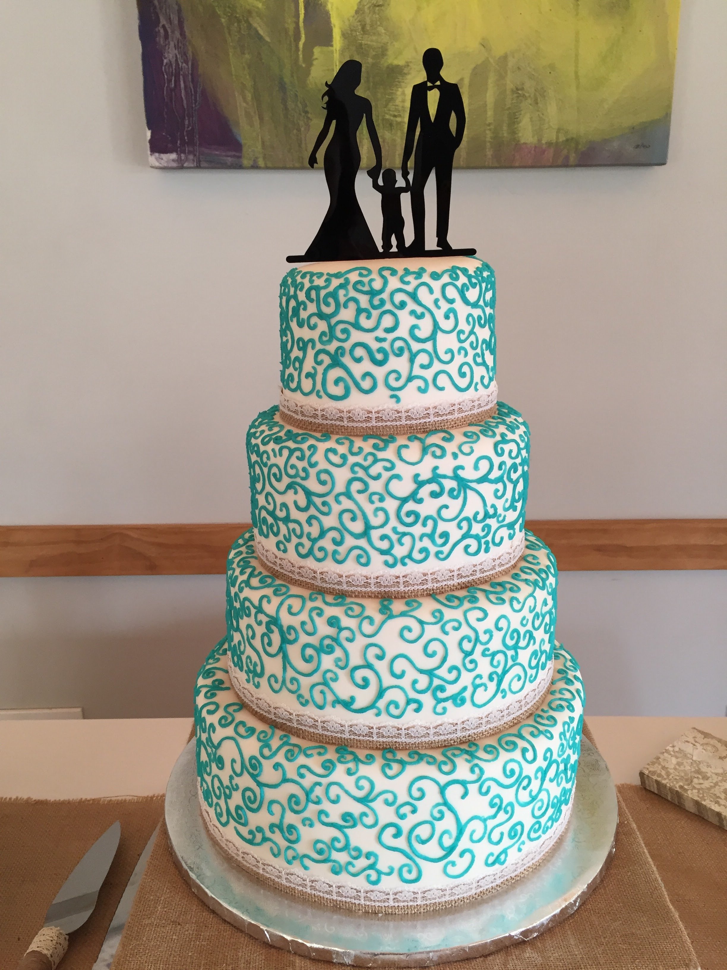 Four-tier white wedding cake with turquoise buttercream scrollwork, lace trim, and family silhouette topper at Juliette Chapel in Dahlonega, GA.