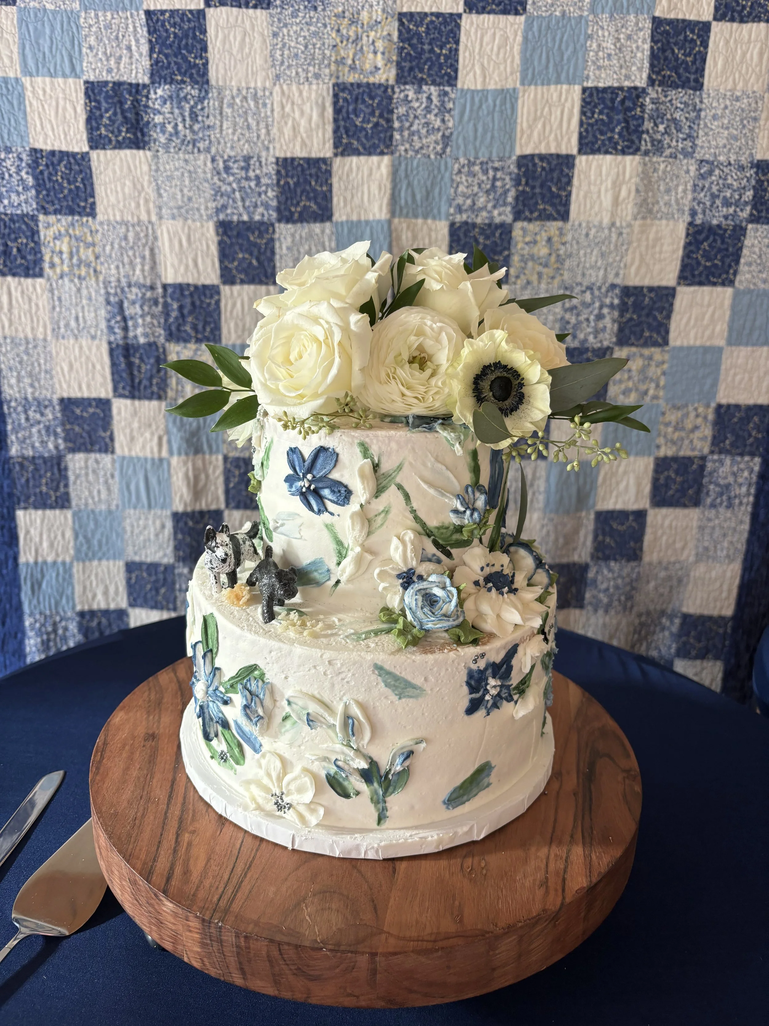 Two-tier buttercream wedding cake with hand-painted blue and white flowers, fresh ivory roses, and greenery at Juliette Chapel in Dahlonega.