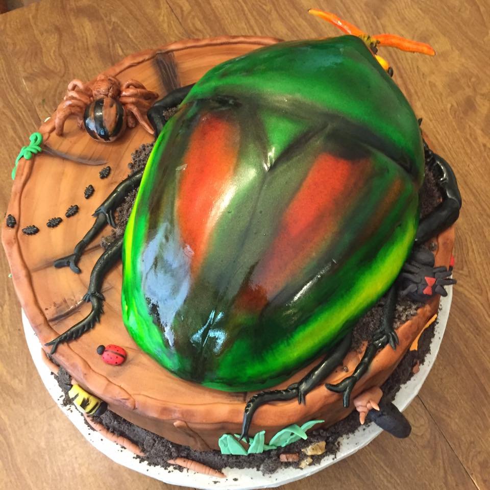 Vibrant beetle sculpted cake on tree stump with detailed edible insects