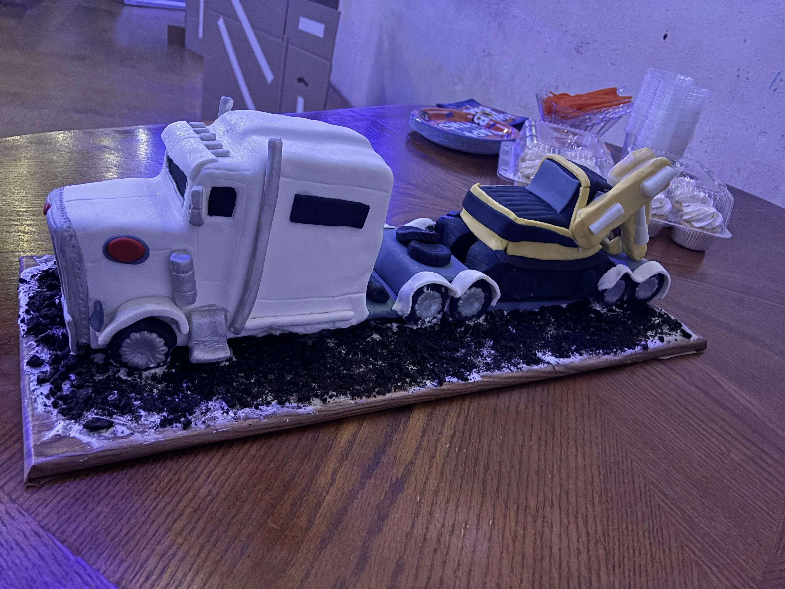 Cake shaped like a semi-truck and a construction vehicle, sitting on a decorated base