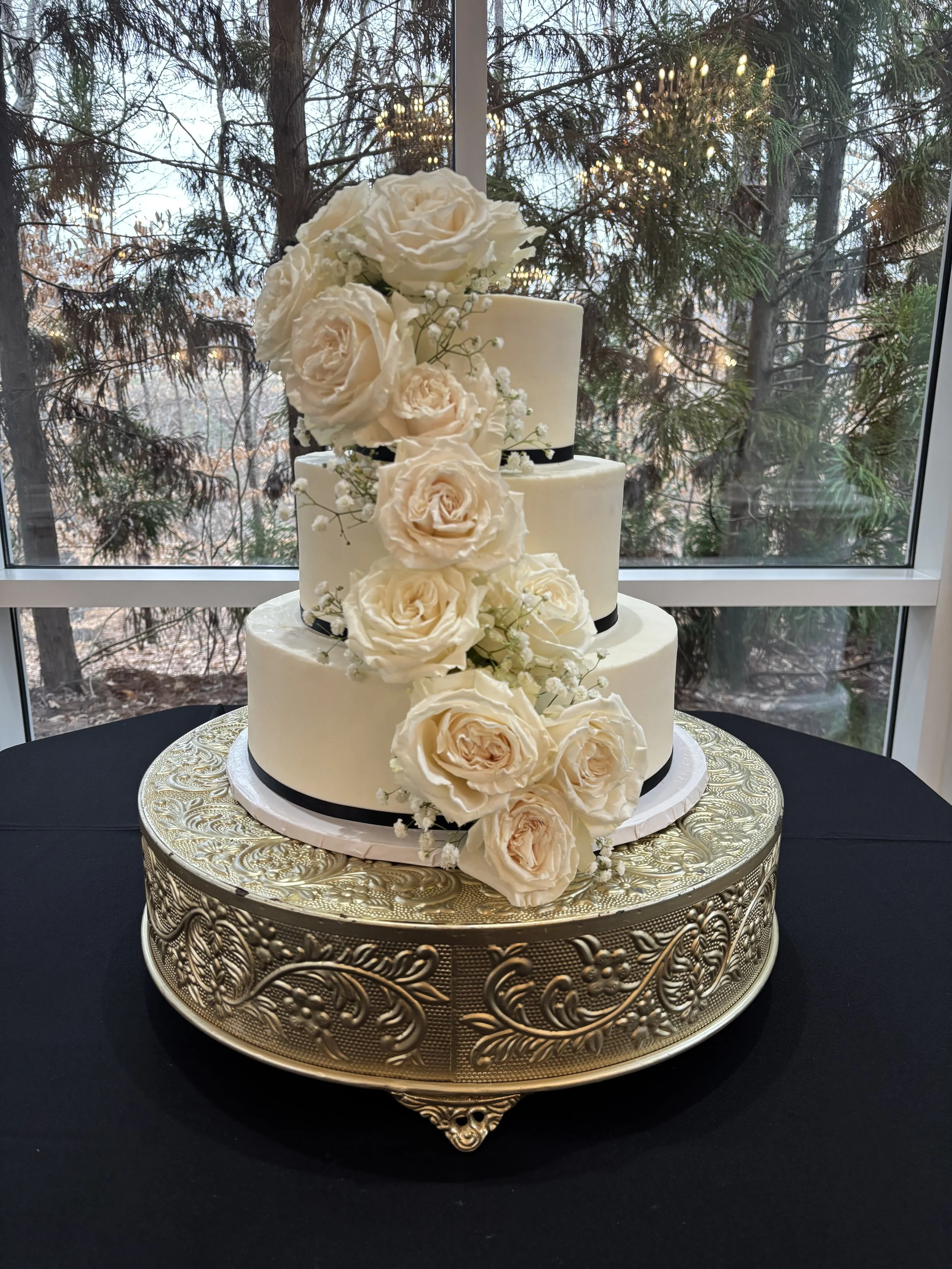 Beautiful three tiered buttercream smooth iced wedding cake with fresh roses and baby's breath and a thin black ribbon at Ashton Gardens Atlanta in Sugar Hill, Georgia