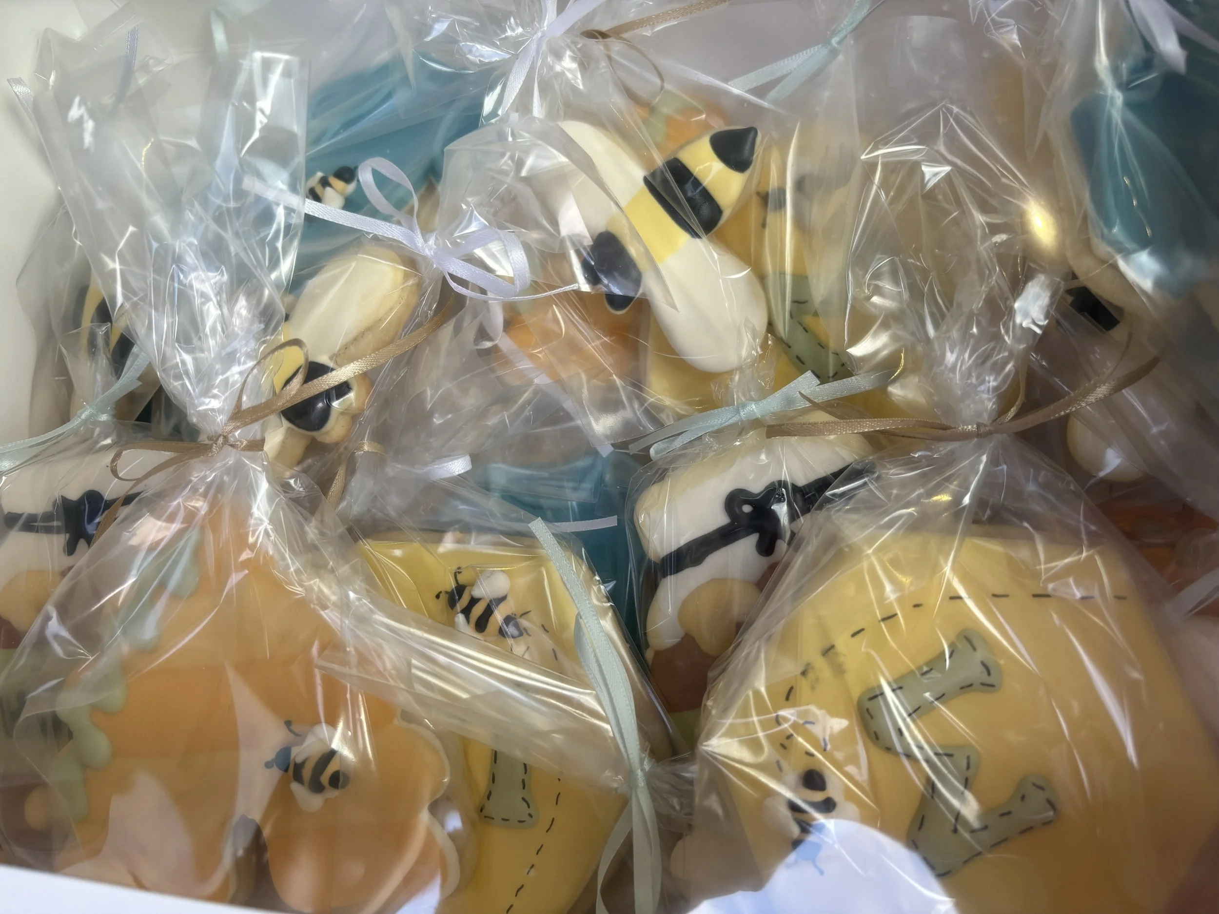 Honey bee and bee hive-shaped decorated cookies wrapped in clear plastic bags with ribbons.