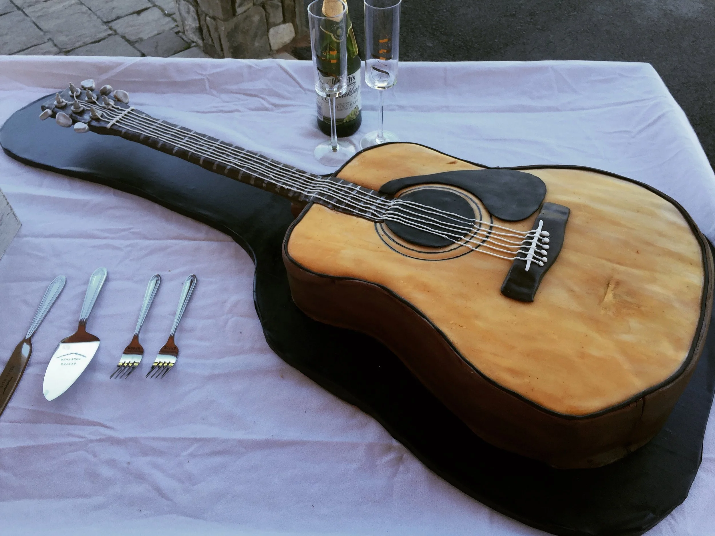 Cake shaped like an acoustic guitar placed on a table with silverware and drinks.