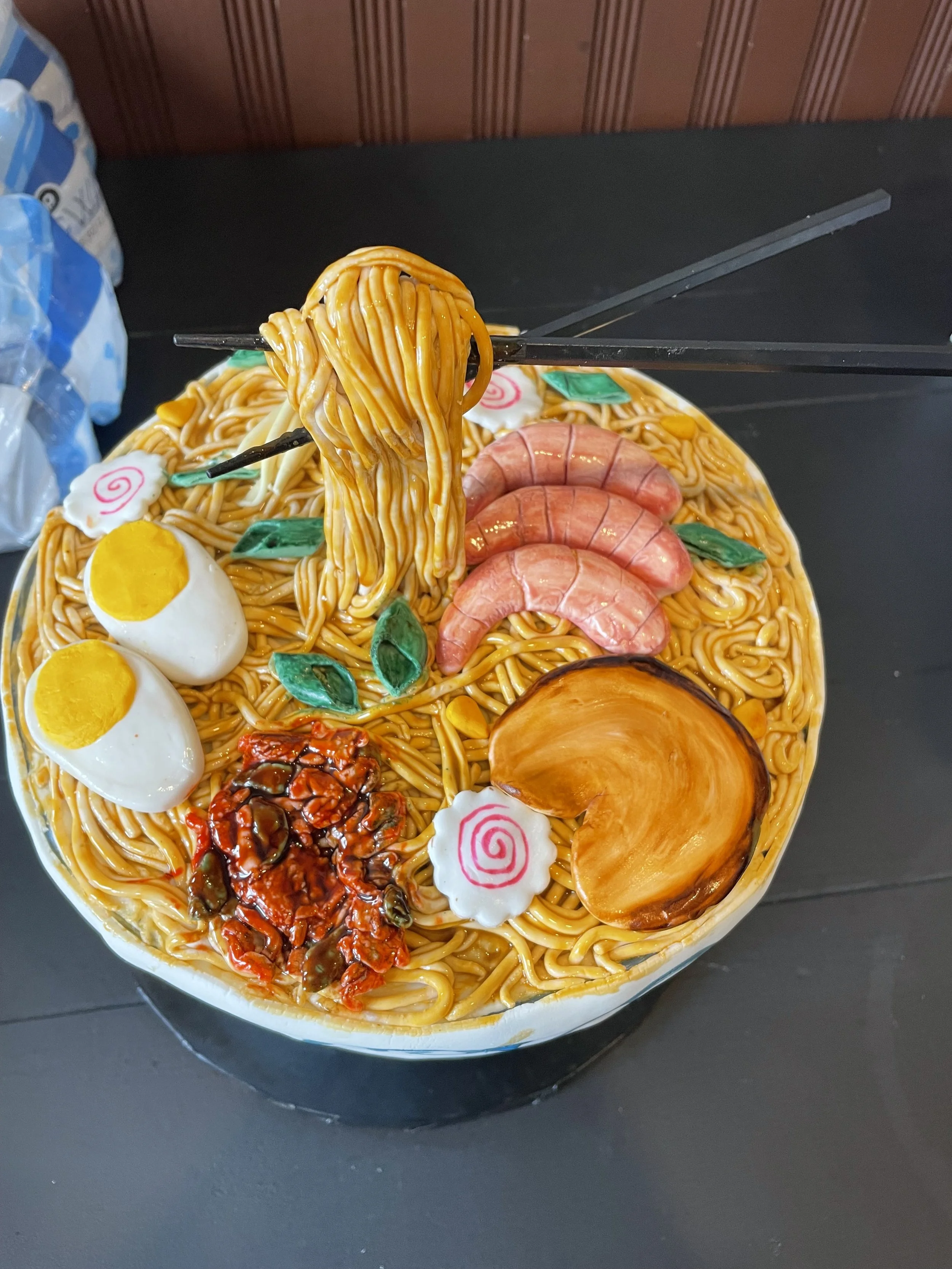 Decorative bowl of ramen cake with noodles, boiled eggs, shrimp, a slice of pumpkin, and Naruto fish cakes.