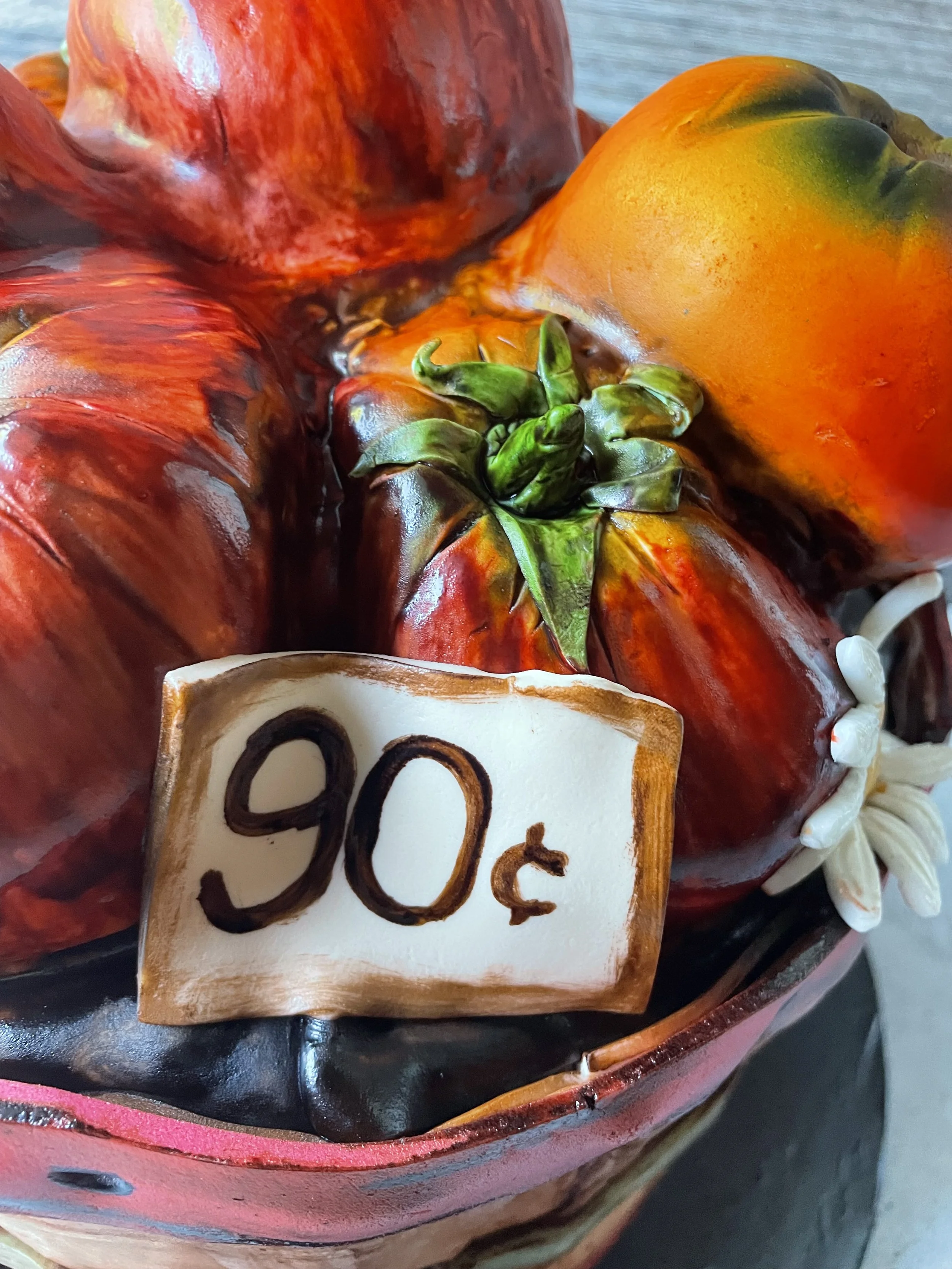 A fondant decorative basket containing cake that looks like painted tomatoes and a flower, with a price tag of 90 cents.