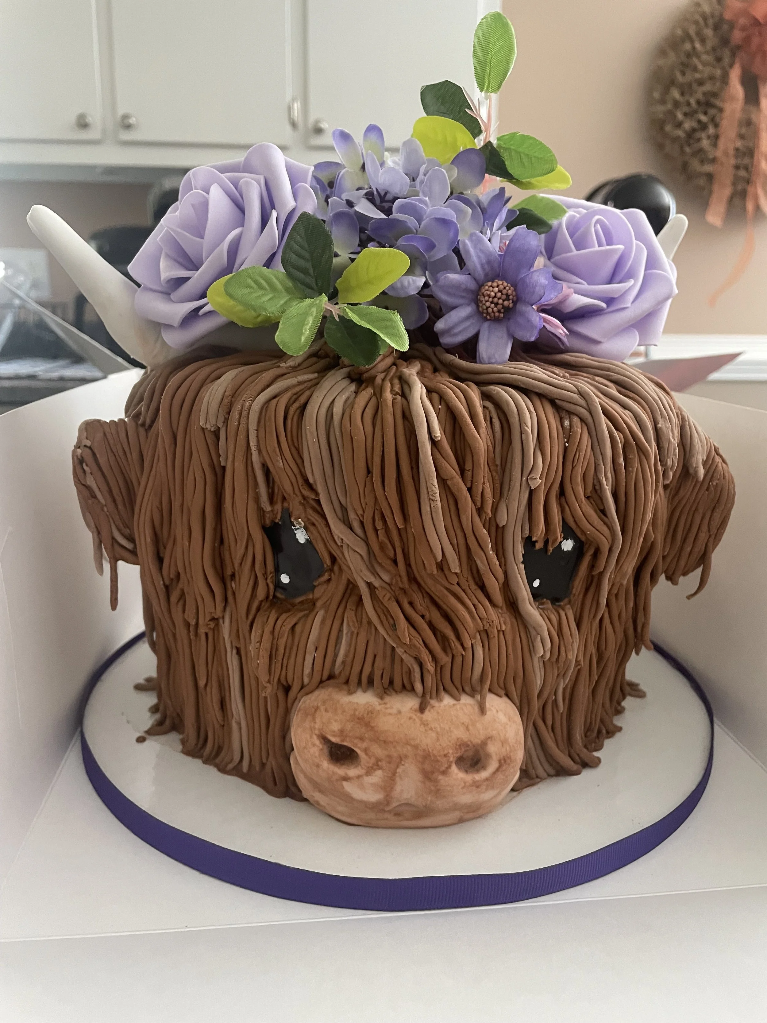 Highland cow cake decorated with purple flowers for a rustic themed celebration.
